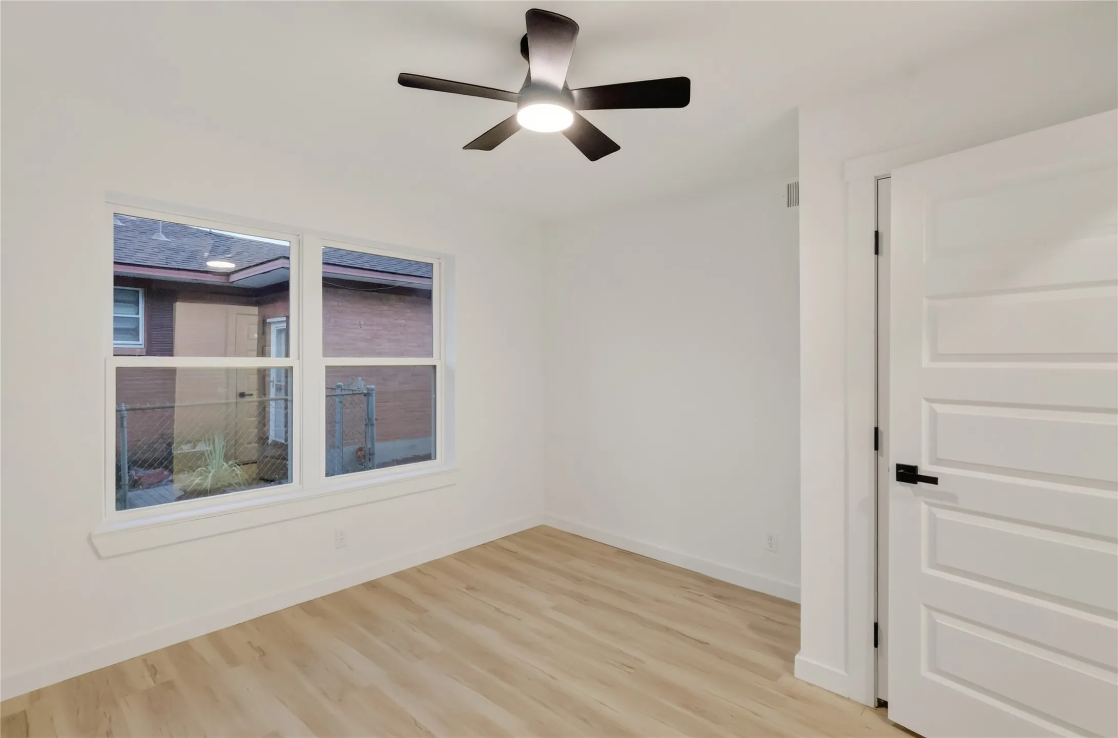 Second Bedroom: Wood-finish flooring, white walls, white trim, modern ceiling fan, and a white paneled door with black hardware