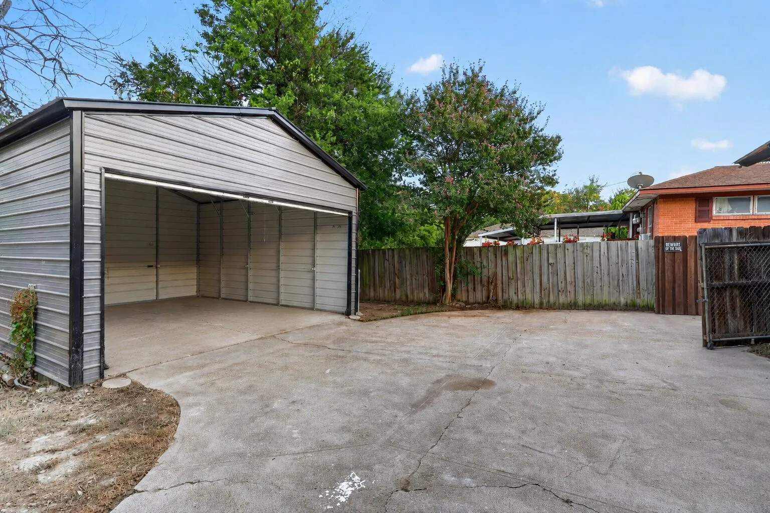 Detached garage featuring a roll-up door and concrete flooring, complemented by a concrete driveway and wood fencing