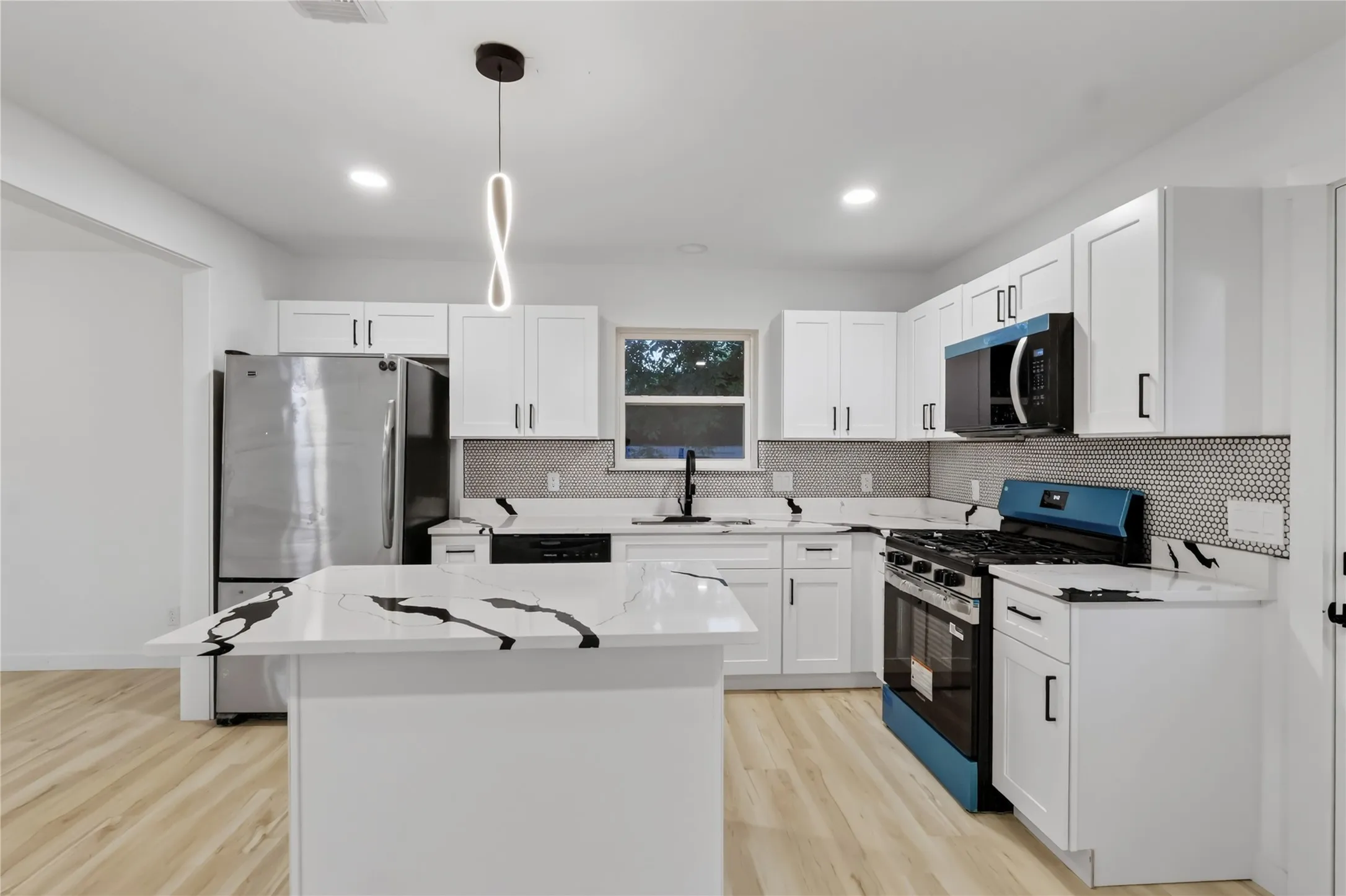 Kitchen featuring white shaker cabinetry, white countertops with dark veining, stainless steel appliances, a geometric tile backsplash, and light wood-finish flooring