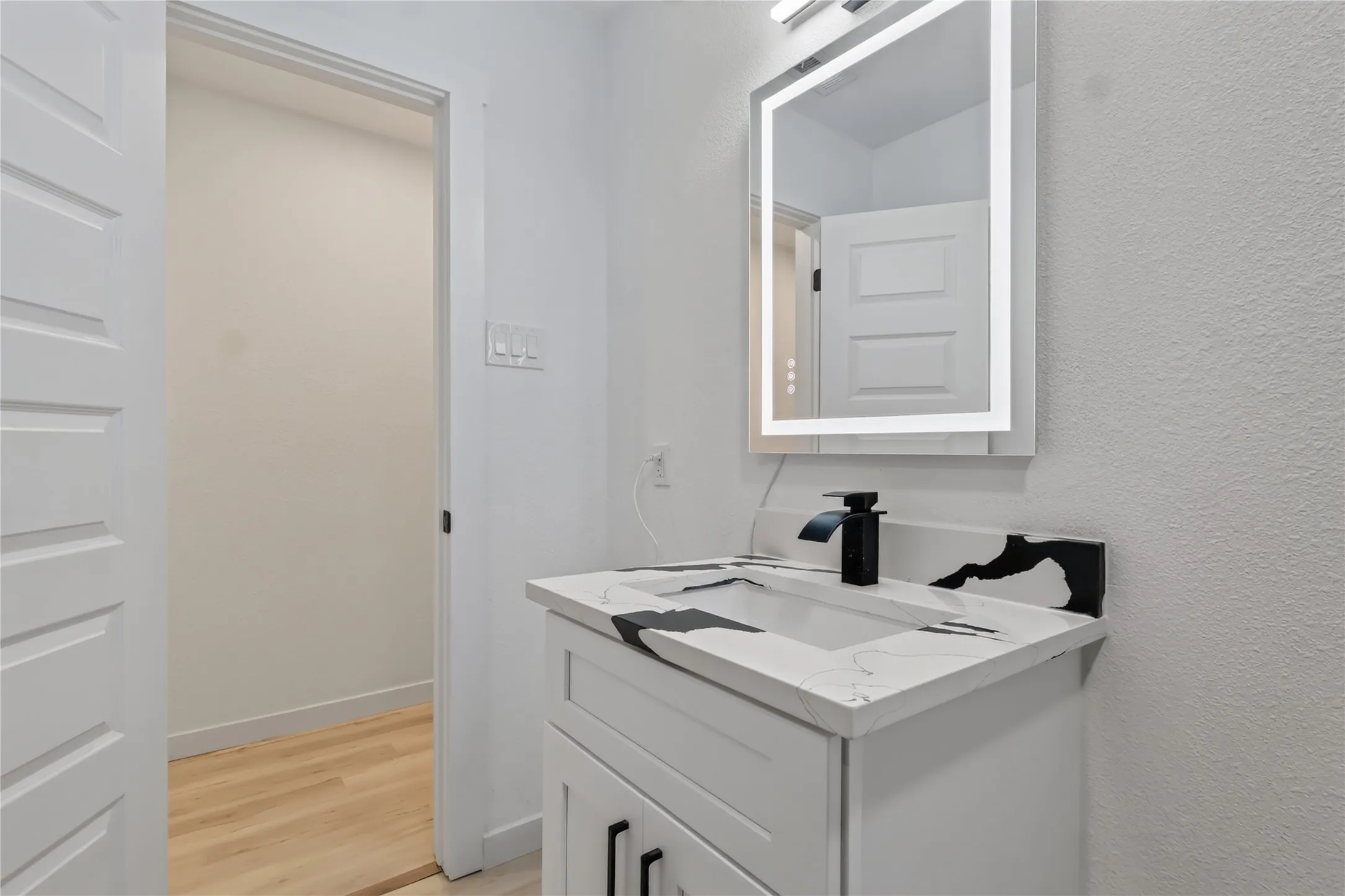 Vanity with integrated sink, black-and-white veined countertop, matte black waterfall faucet, and illuminated mirror