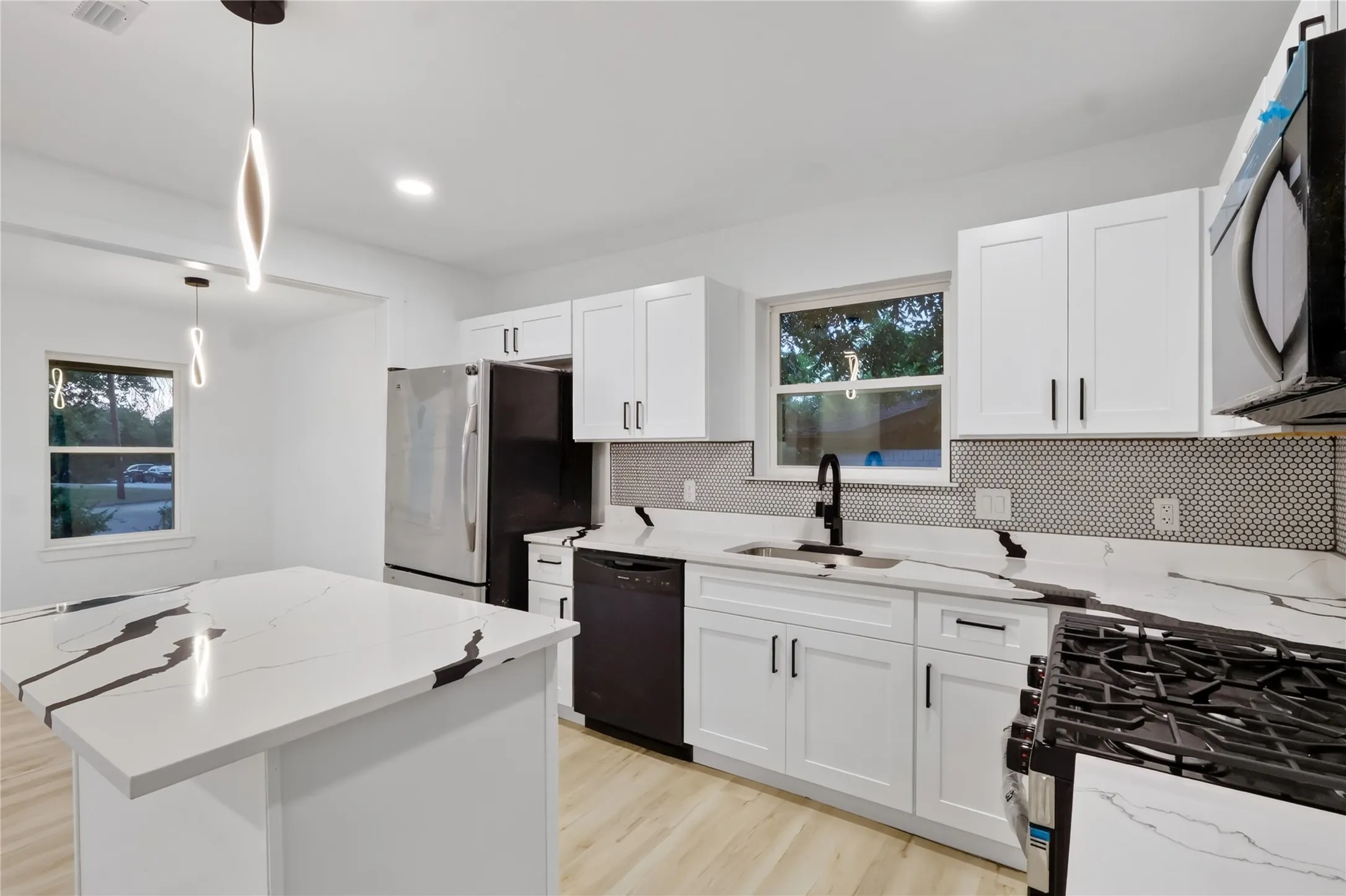 Kitchen featuring white cabinetry, a kitchen island with a white and black veined countertop, pendant lighting, wood-finish flooring, and a mosaic tile backsplash