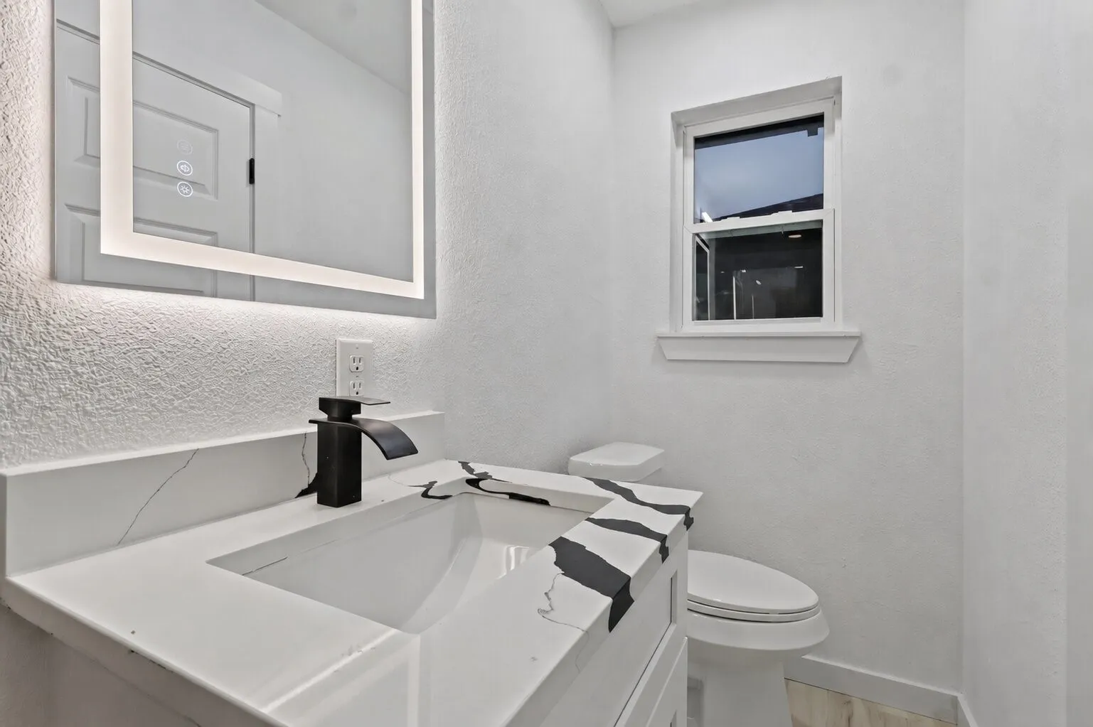 Built-in vanity with integrated sink, sleek matte black faucet, illuminated mirror, and a single-pane window