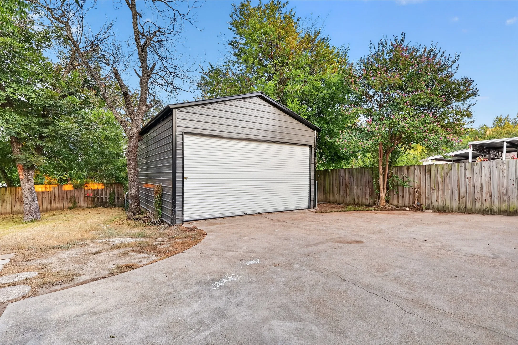 Detached metal garage with a roll-up door, concrete driveway, and a wood privacy fence