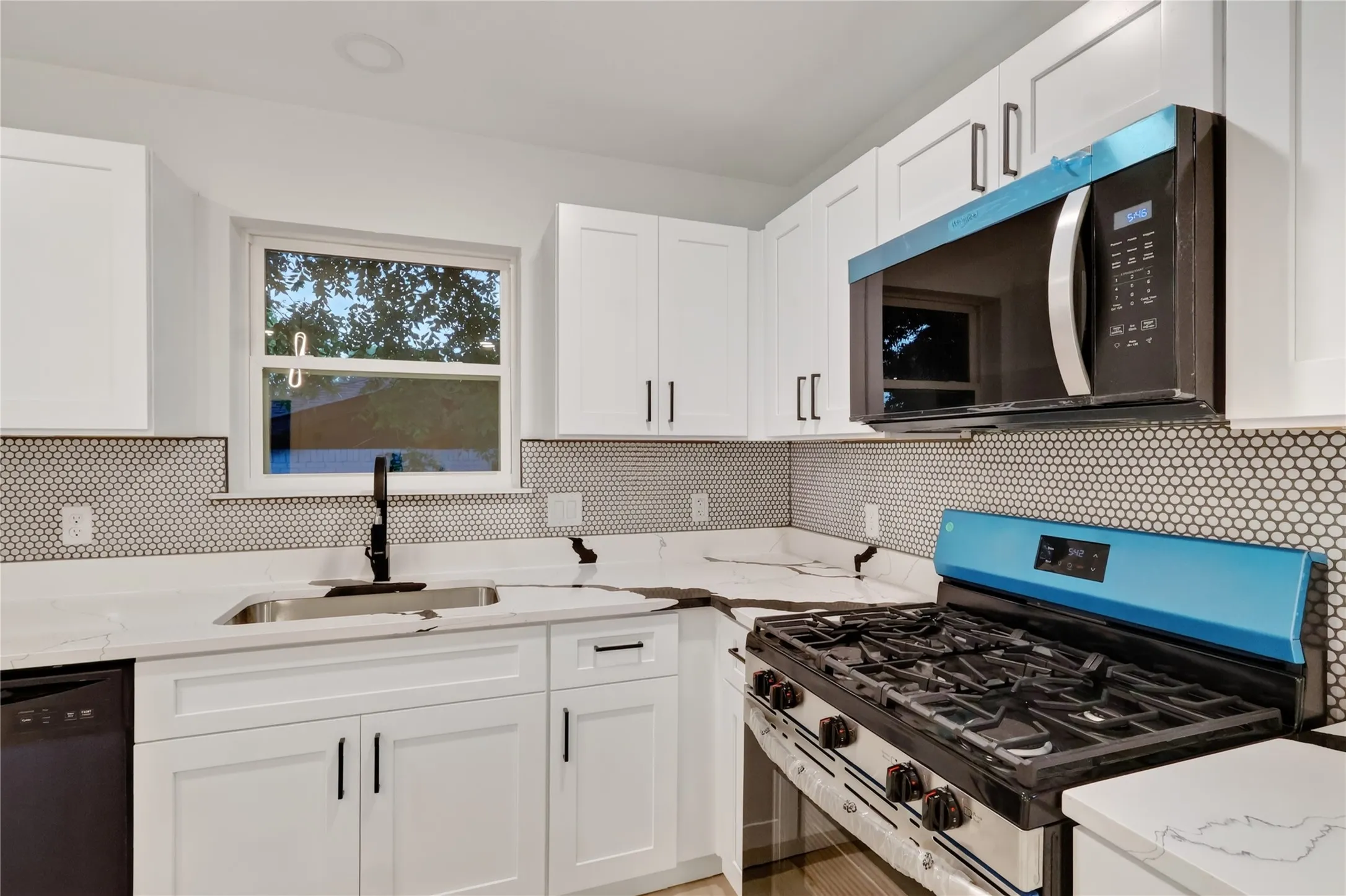 White shaker cabinetry, honeycomb tile backsplash, stainless steel sink with matte black faucet, built-in microwave, and stainless steel gas range