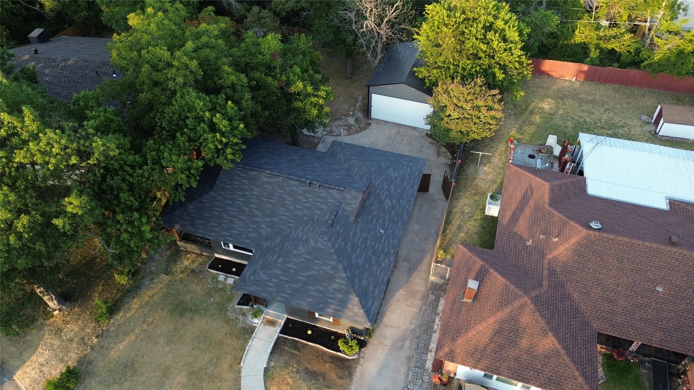 Main structure with dark shingle roof, extensive green landscaping, and attached garage