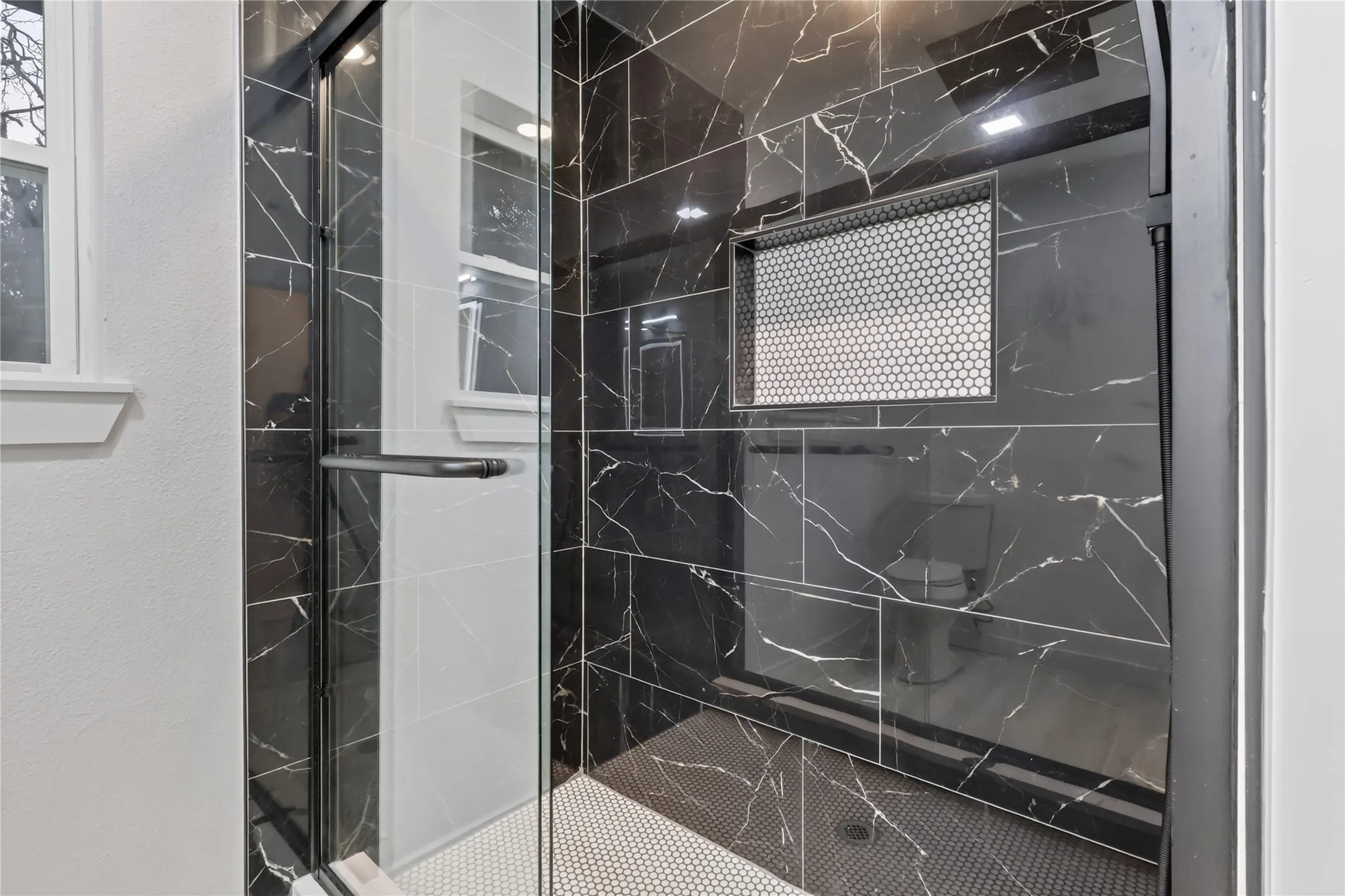 Frameless glass shower enclosure with black framing, black marbled tile shower walls, and a black hexagon tile shower floor