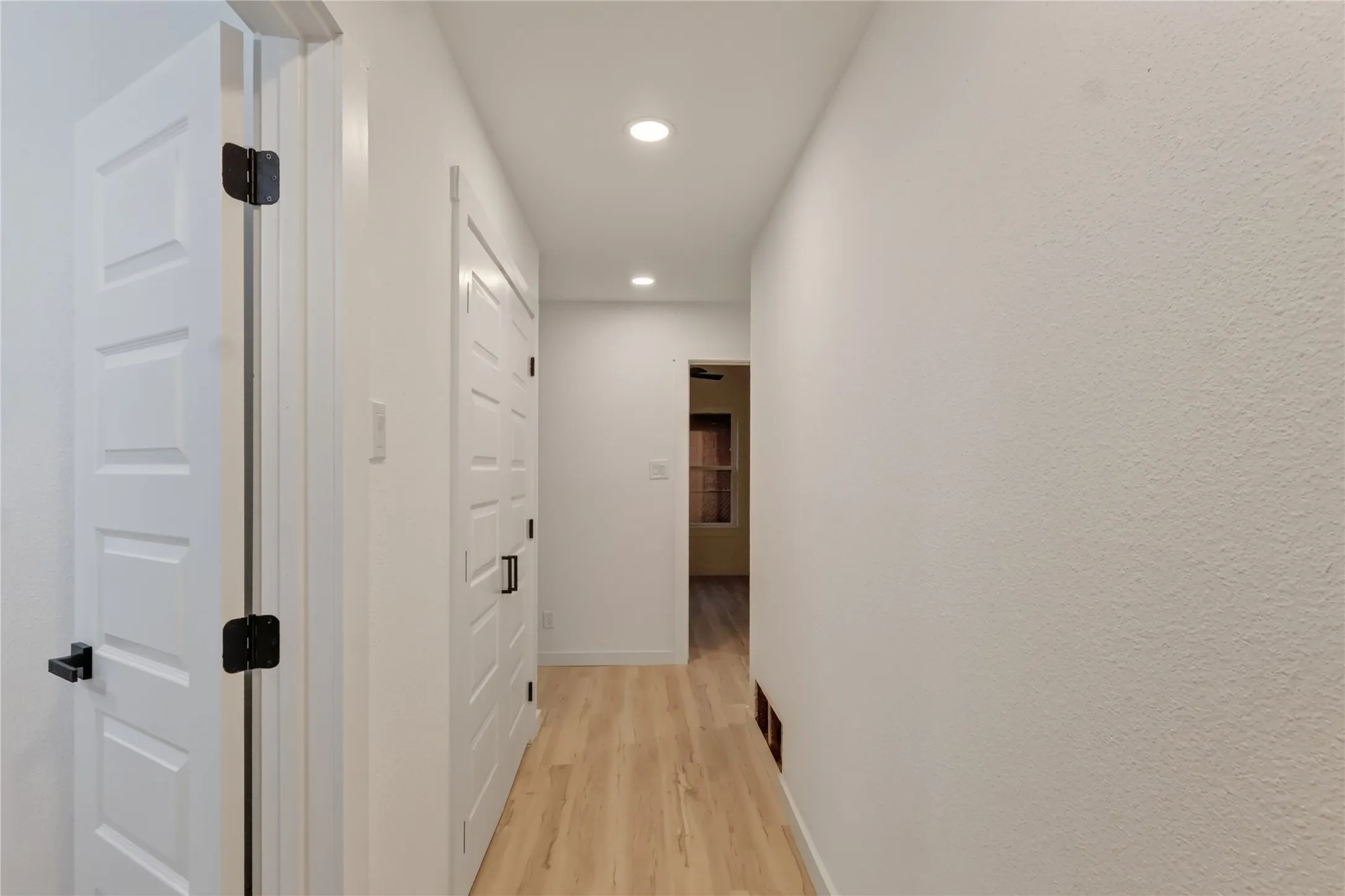 Hallway featuring wood-finish flooring, recessed lighting, and panel doors with matte black hardware