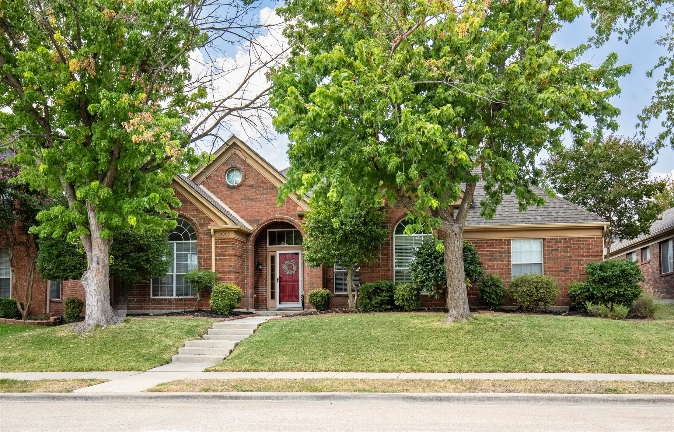 Exterior features beautiful curb appeal including mature trees providing shade, lush landscaping, and glass storm door to entry.