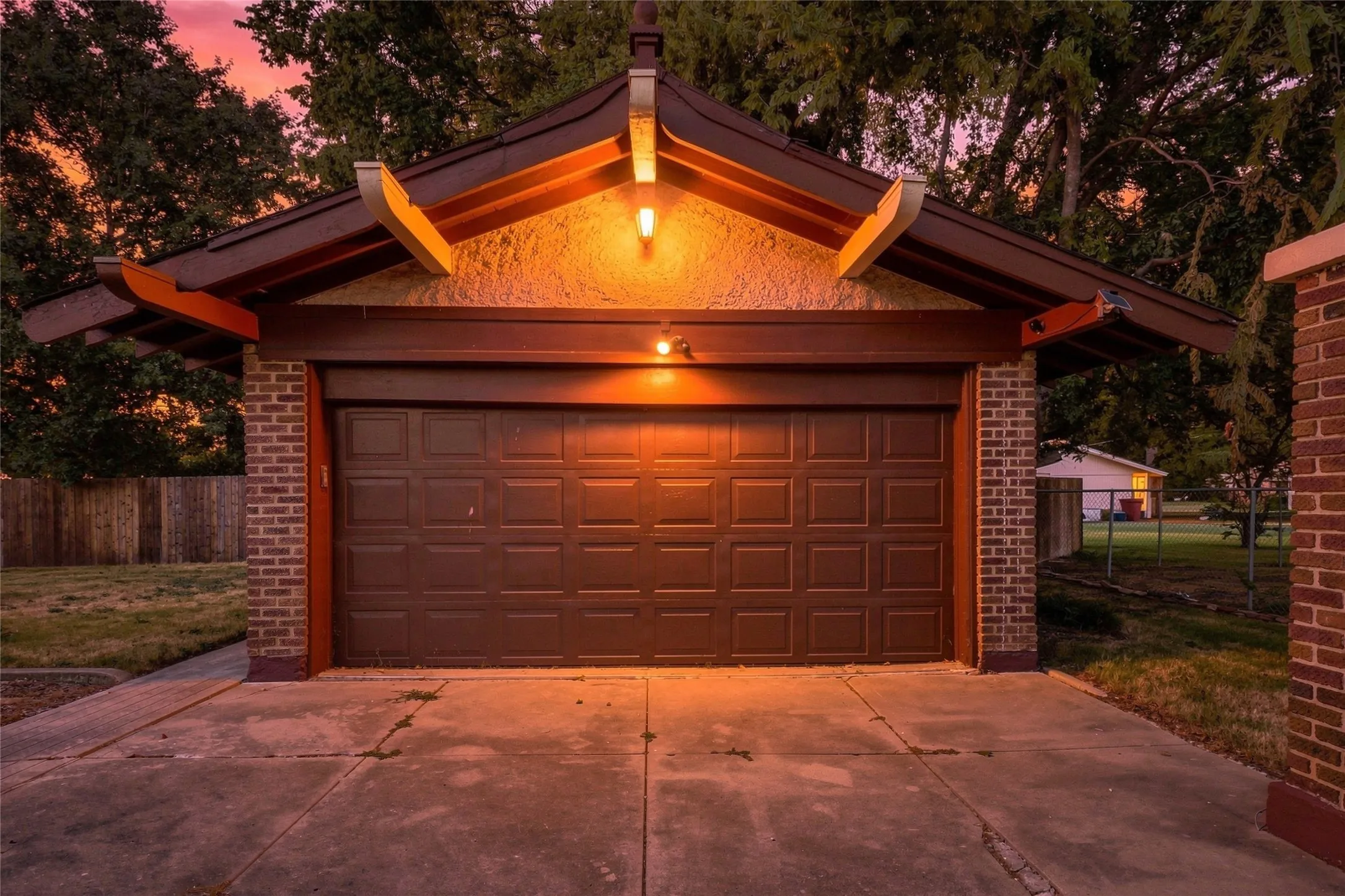 Detached garage featuring a panel-style door, brick columns, stucco facade, and an architectural overhang