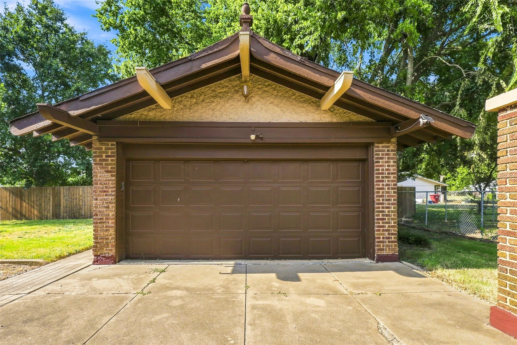 Detached garage with a brown panel door, brick facade, and stucco siding