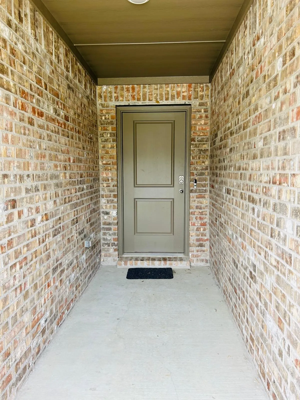Brick exterior entry with covered porch and a panel-style door featuring a smart lock