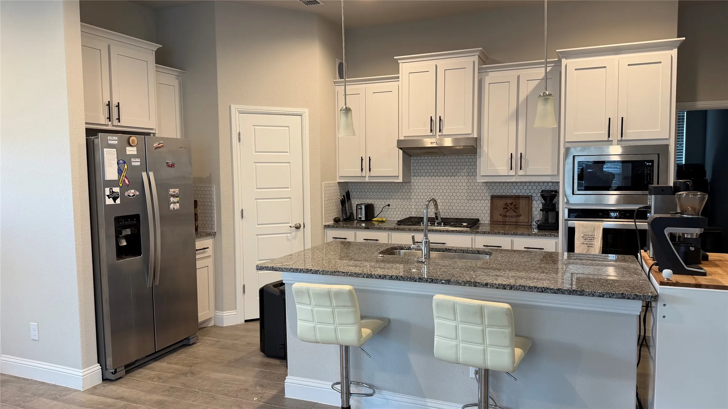 Kitchen featuring white shaker cabinetry, stainless steel appliances, speckled stone countertops, a hexagonal tile backsplash, and wood-finish flooring