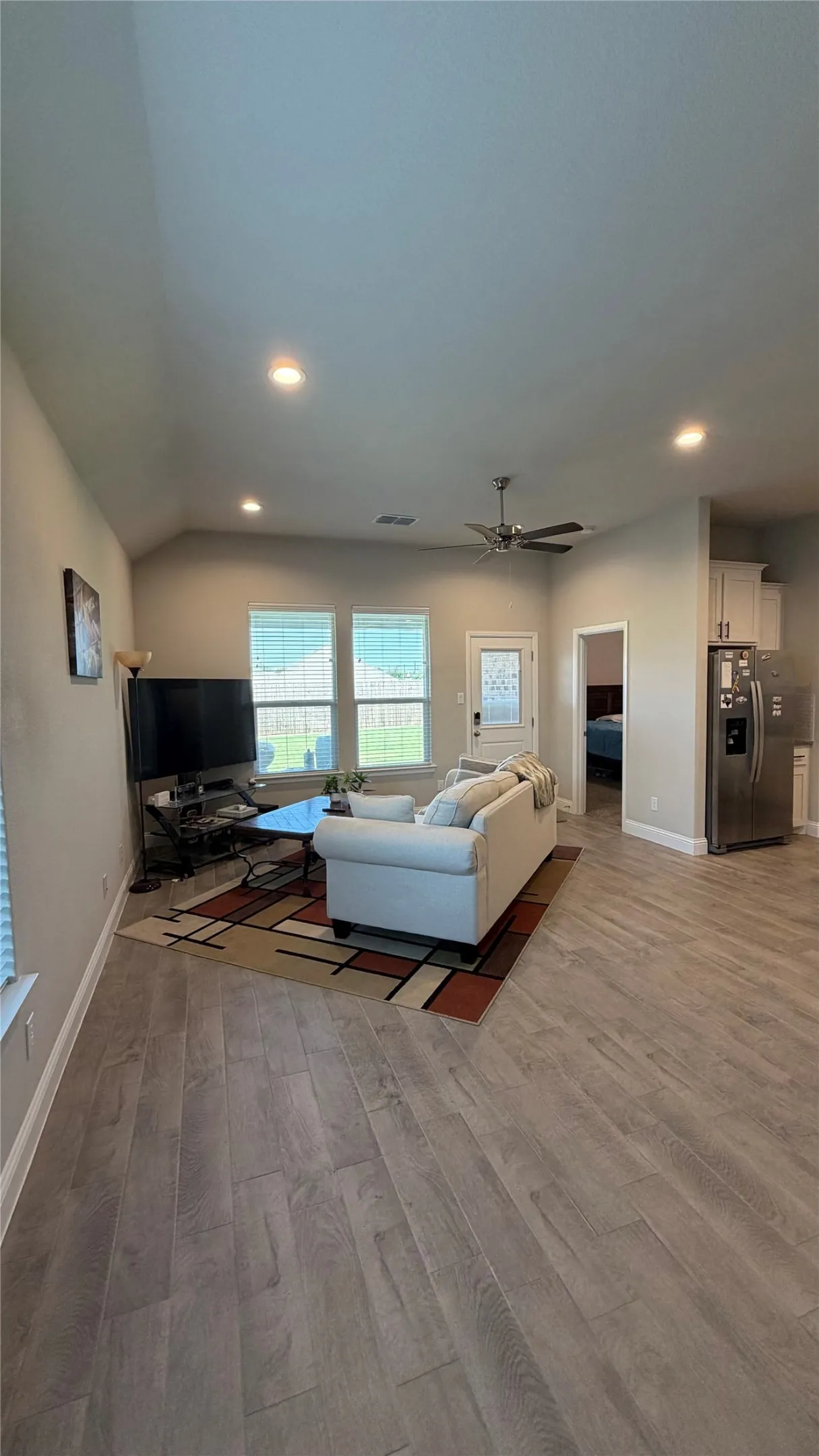 Vaulted ceiling with recessed lighting, wood-finish flooring, three transom windows, ceiling fan, and white cabinetry with stainless steel appliances