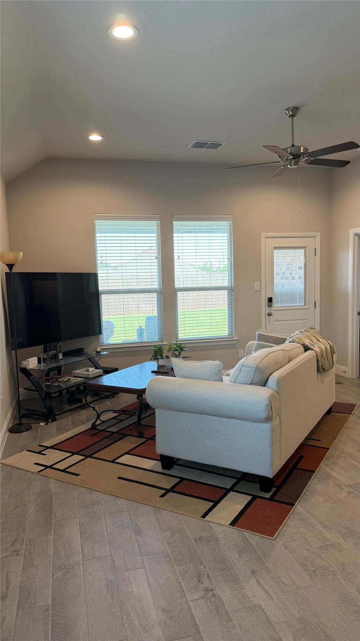 Vaulted ceiling, recessed lighting, ceiling fan, wood-finish flooring, and a rear door with decorative glass