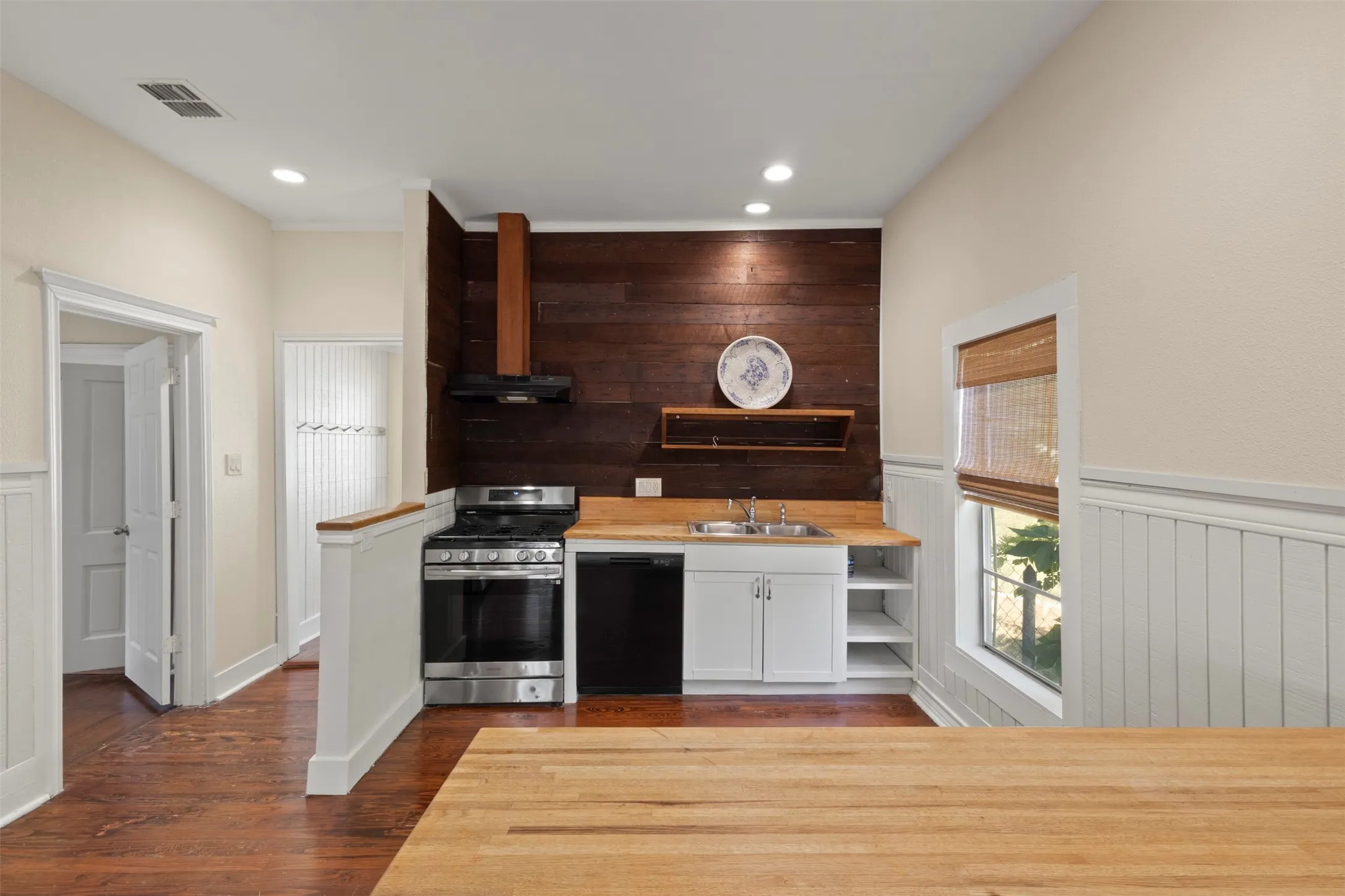 Full kitchen featuring wood-finish flooring, white wainscoting, wood countertops, stainless steel appliances (incl. fridge/freezer + microwave), and recessed lighting