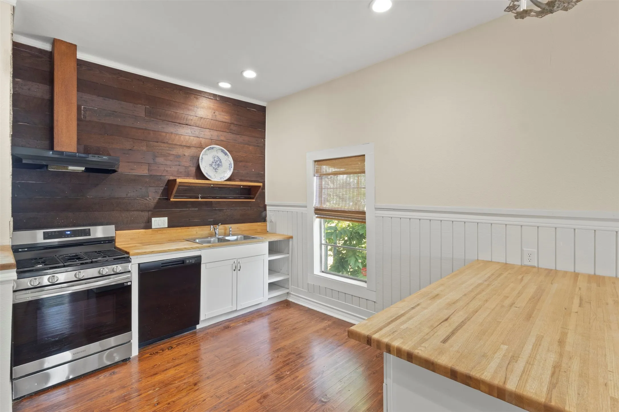 Wood-finish flooring, wood plank accent wall, stainless steel range with range hood, white cabinetry, and light wood countertops