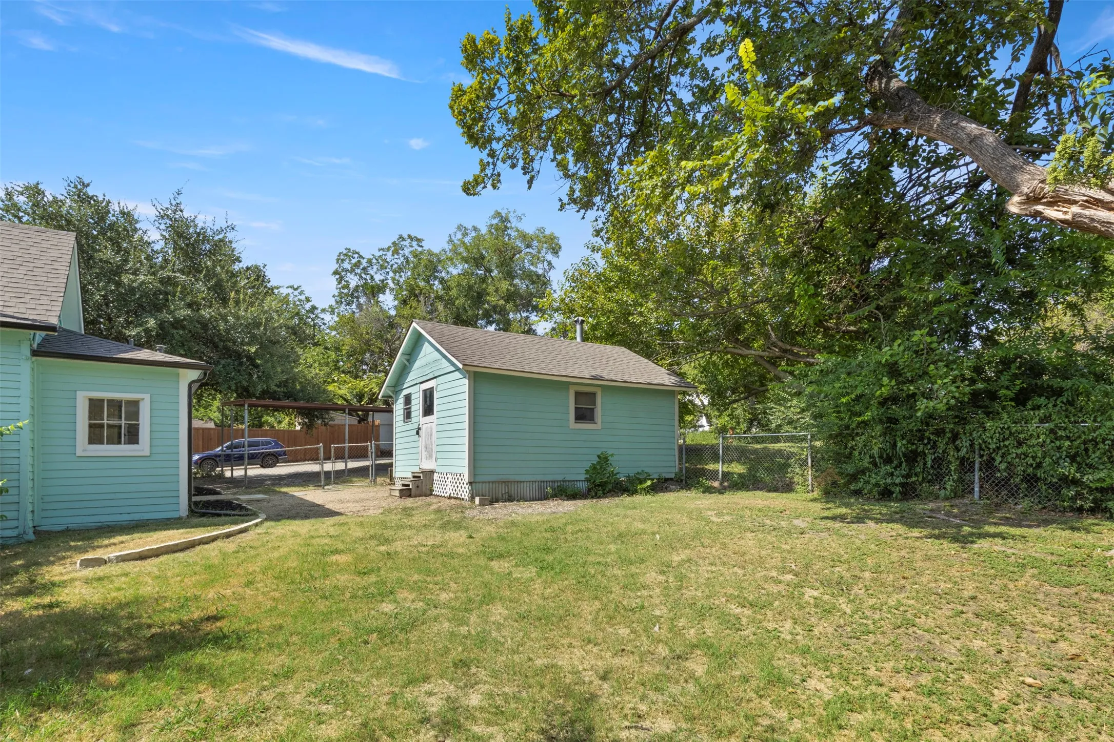Expansive yard space featuring a standalone shed with siding, a separate structure with siding, and mature perimeter trees