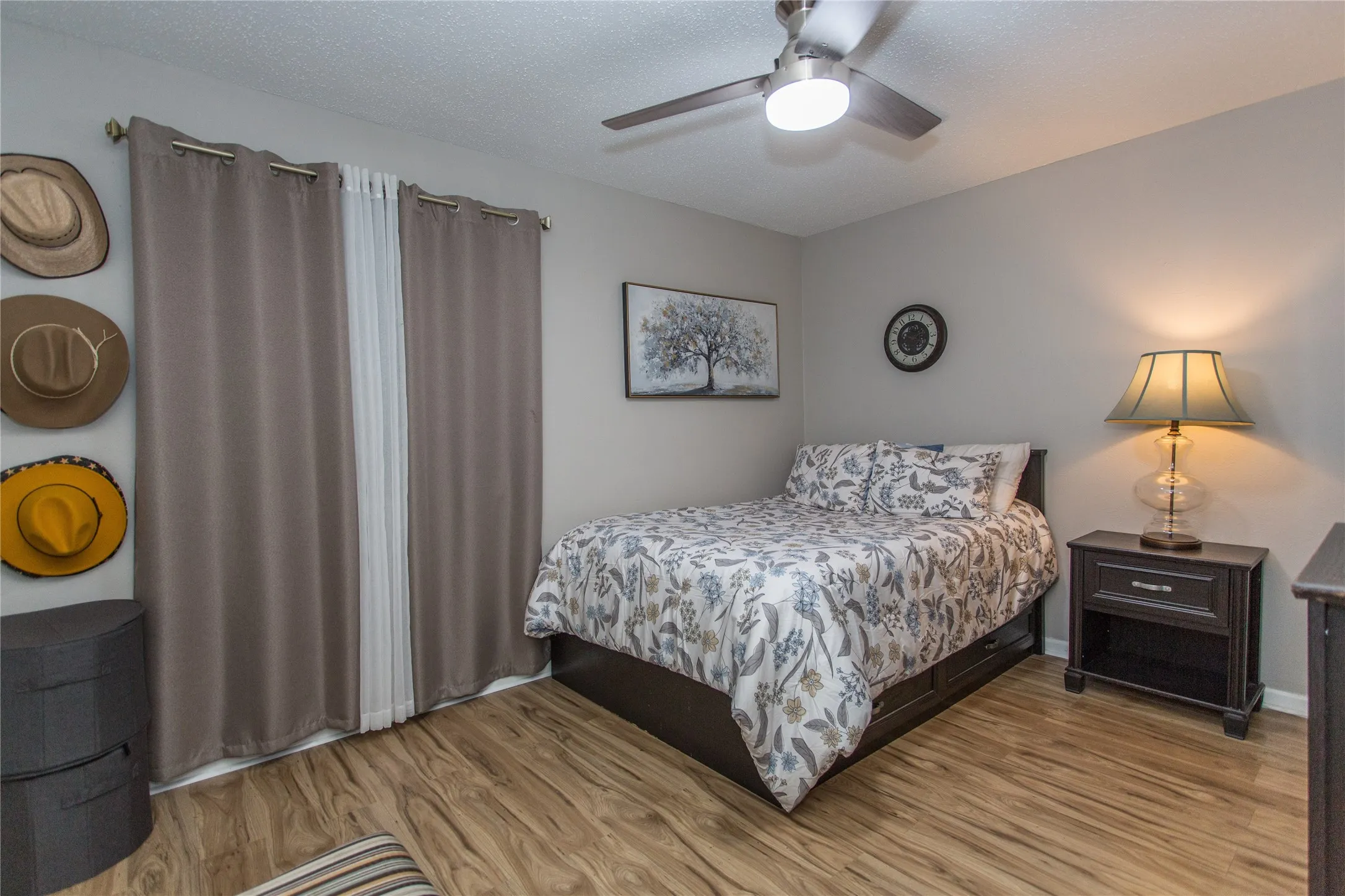Bedroom with wood-finish flooring, a ceiling fan with integrated lighting, and a window with opaque drapes