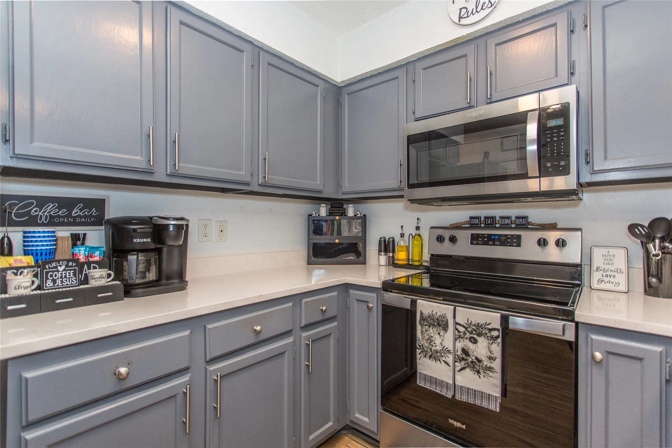 Kitchen featuring gray shaker-style cabinetry with silver hardware, light-toned countertops, a stainless steel over-the-range microwave, and a stainless steel electric range