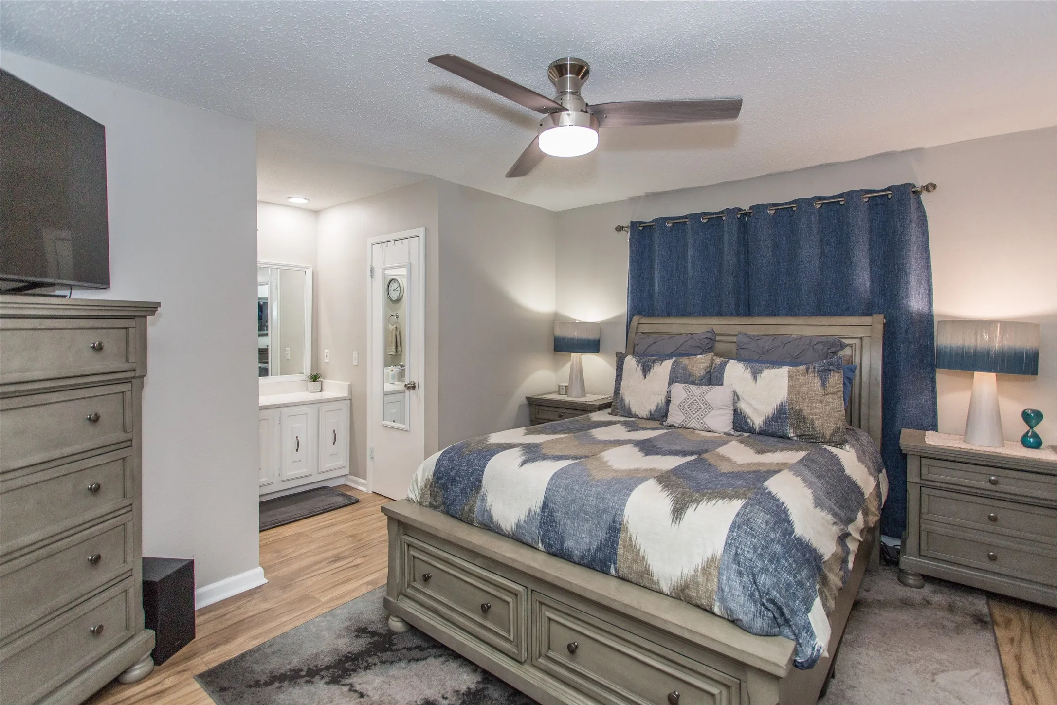 Bedroom featuring wood-finish flooring, a ceiling fan with integrated lighting, and direct access to a vanity area with a built-in cabinet and mirror