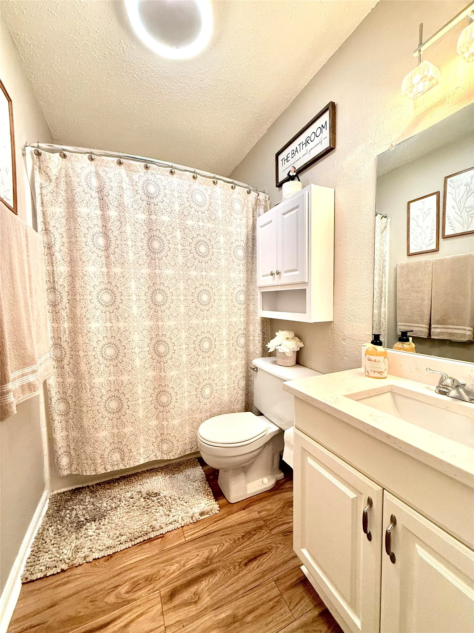 Bathroom featuring wood-finish flooring, a white vanity with cabinet storage, a white toilet, and an overhead storage cabinet