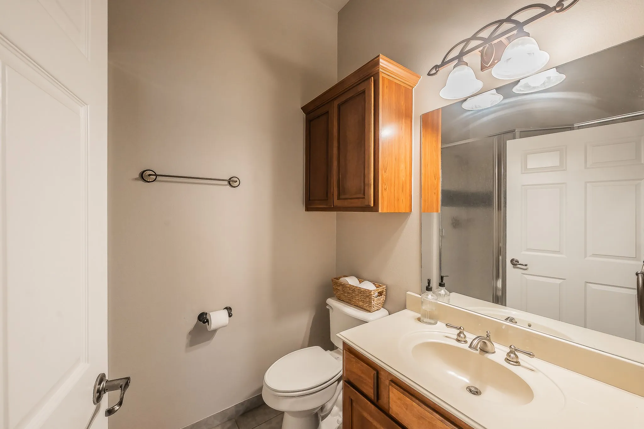 Bathroom featuring a wood-finish vanity with an integrated sink, a large mirror, and a wall-mounted light fixture