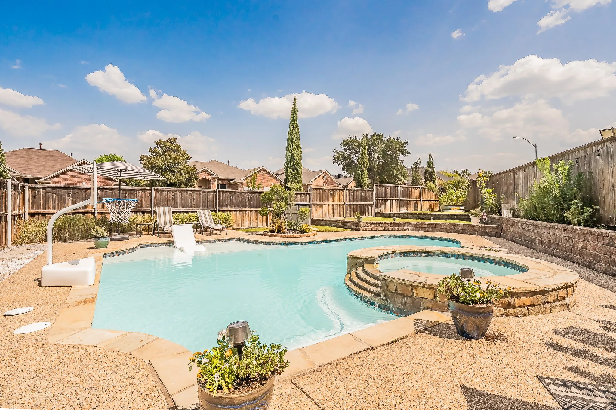 Outdoor pool and integrated spa with stone surround, complemented by a wooden privacy fence and tiered retaining wall