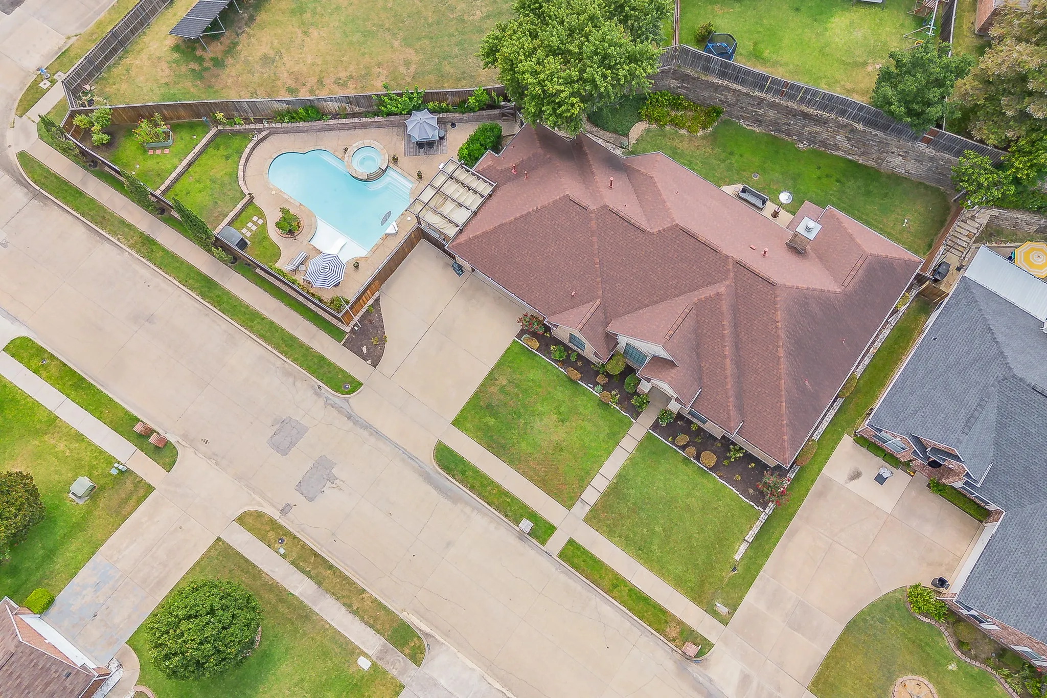 Curved swimming pool with an integrated spa, expansive paver patio, attached pergola, and manicured landscaping