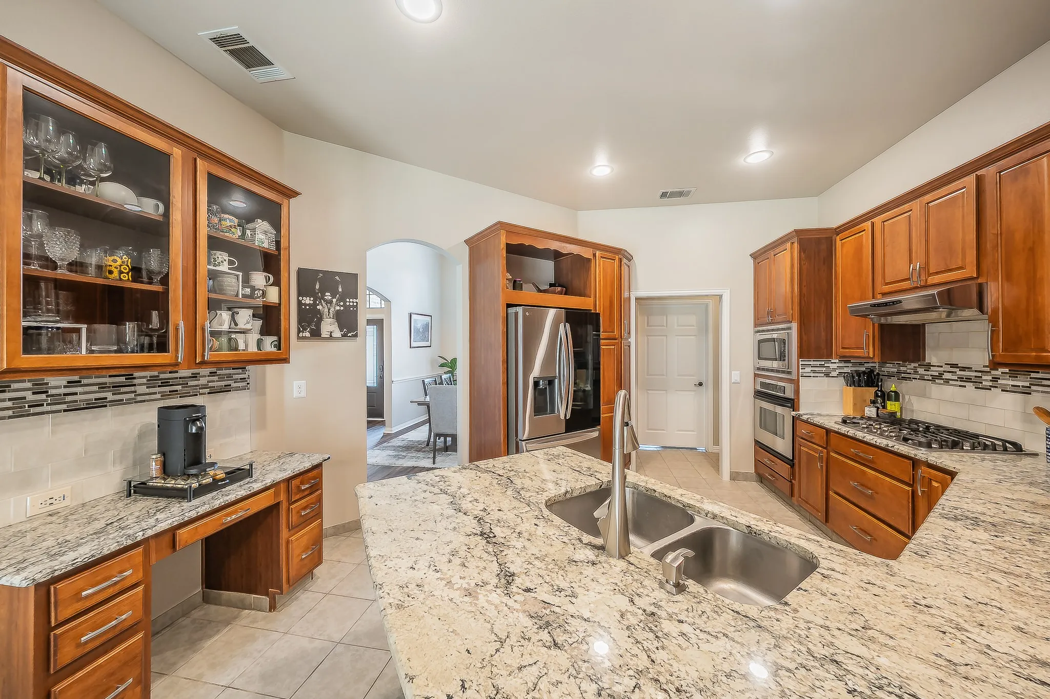 Kitchen featuring dual basin stainless steel sink, light-toned countertops, wood cabinetry, tile flooring, and integrated stainless steel appliances