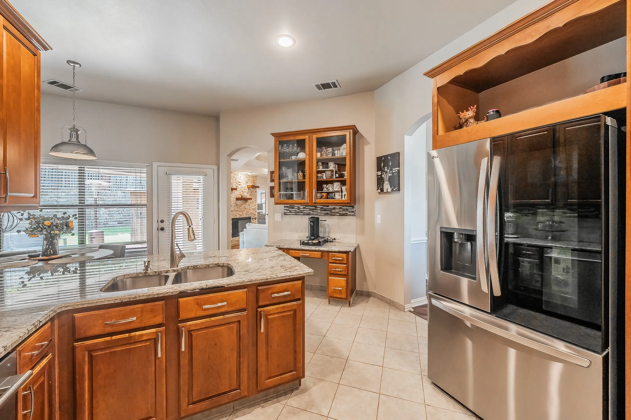 Kitchen featuring stainless steel appliances, granite countertops, tile flooring, wood cabinetry, and an integrated desk area