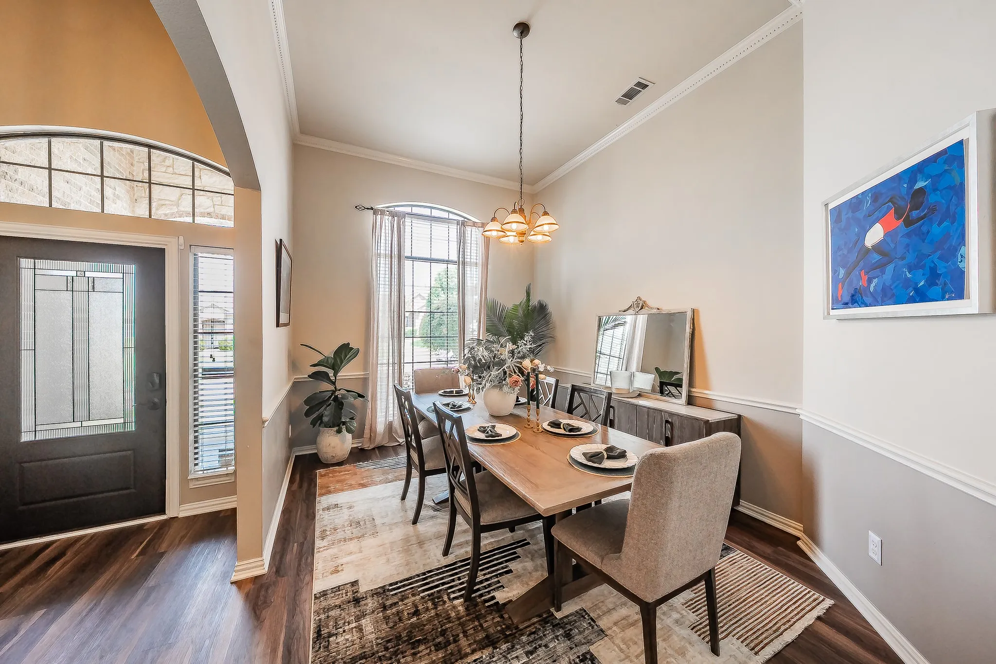 Hardwood-finish flooring, decorative entry door with frosted glass panels, arched transom window, crown molding, and a chandelier