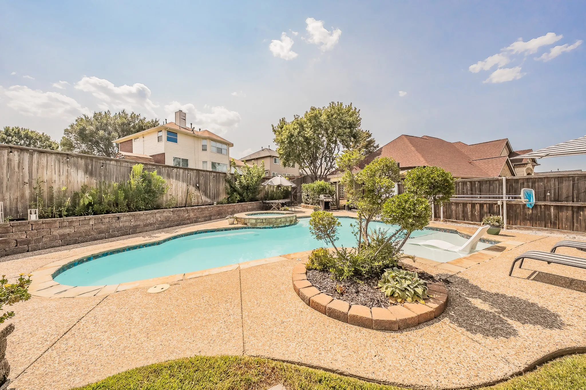 Swimming pool with integrated spa and sun shelf, surrounded by a flagstone-edged concrete patio and a raised wooden fence