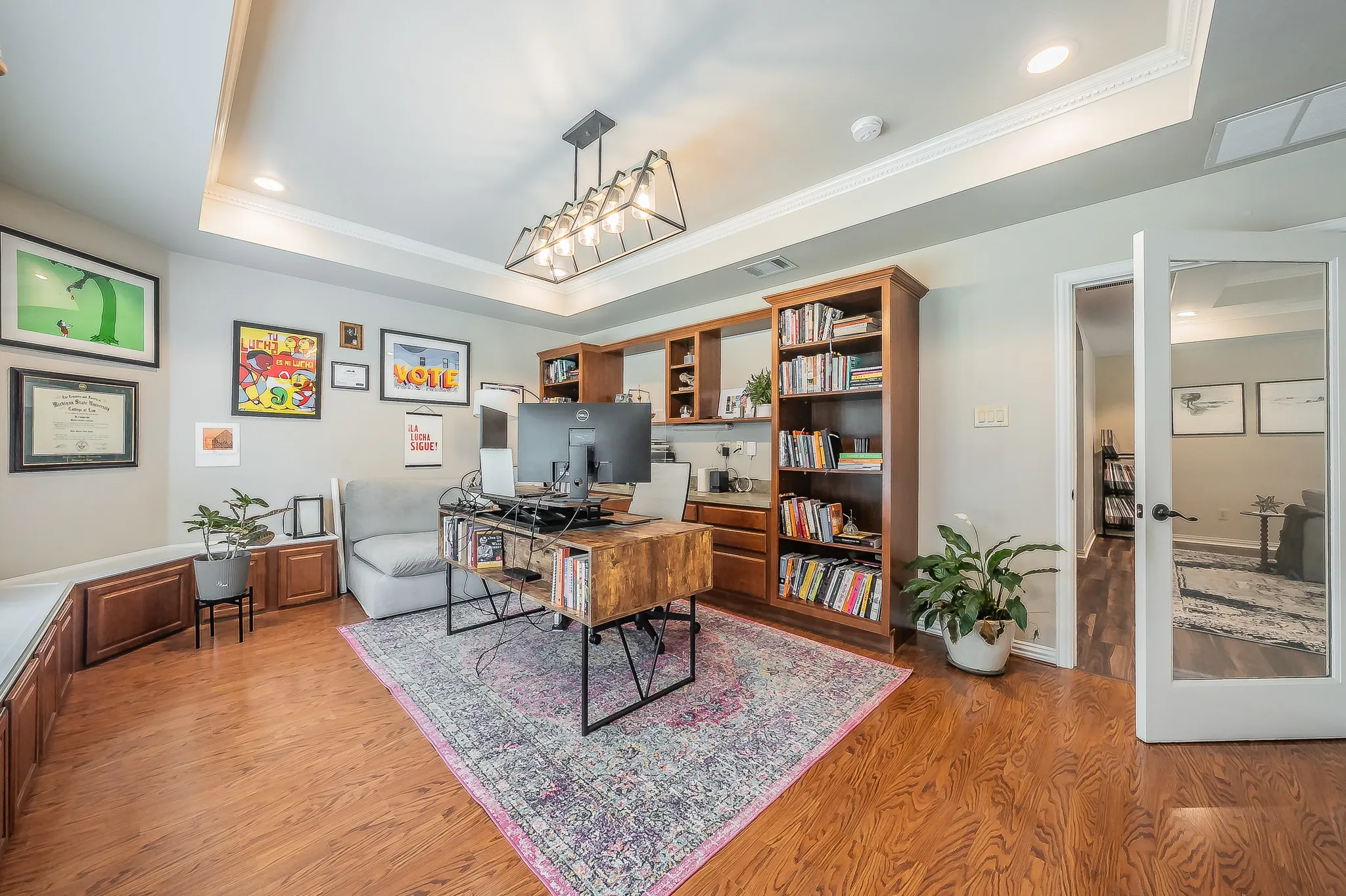 Wood-finish flooring, built-in cabinetry, tray ceiling with crown molding, and a modern chandelier