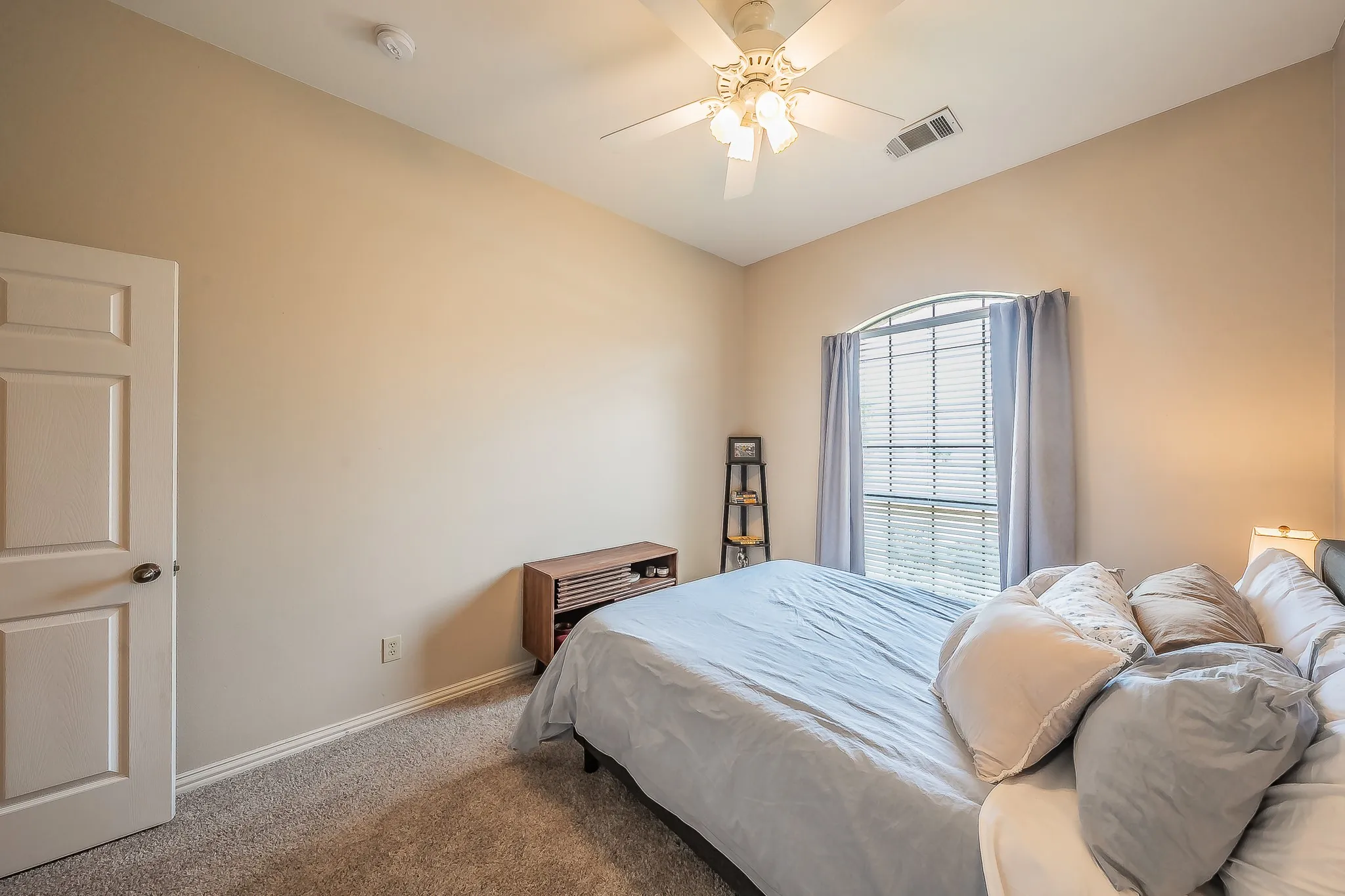 Arch-top window with blinds, ceiling fan with integrated lighting, neutral-toned walls, and carpeted flooring