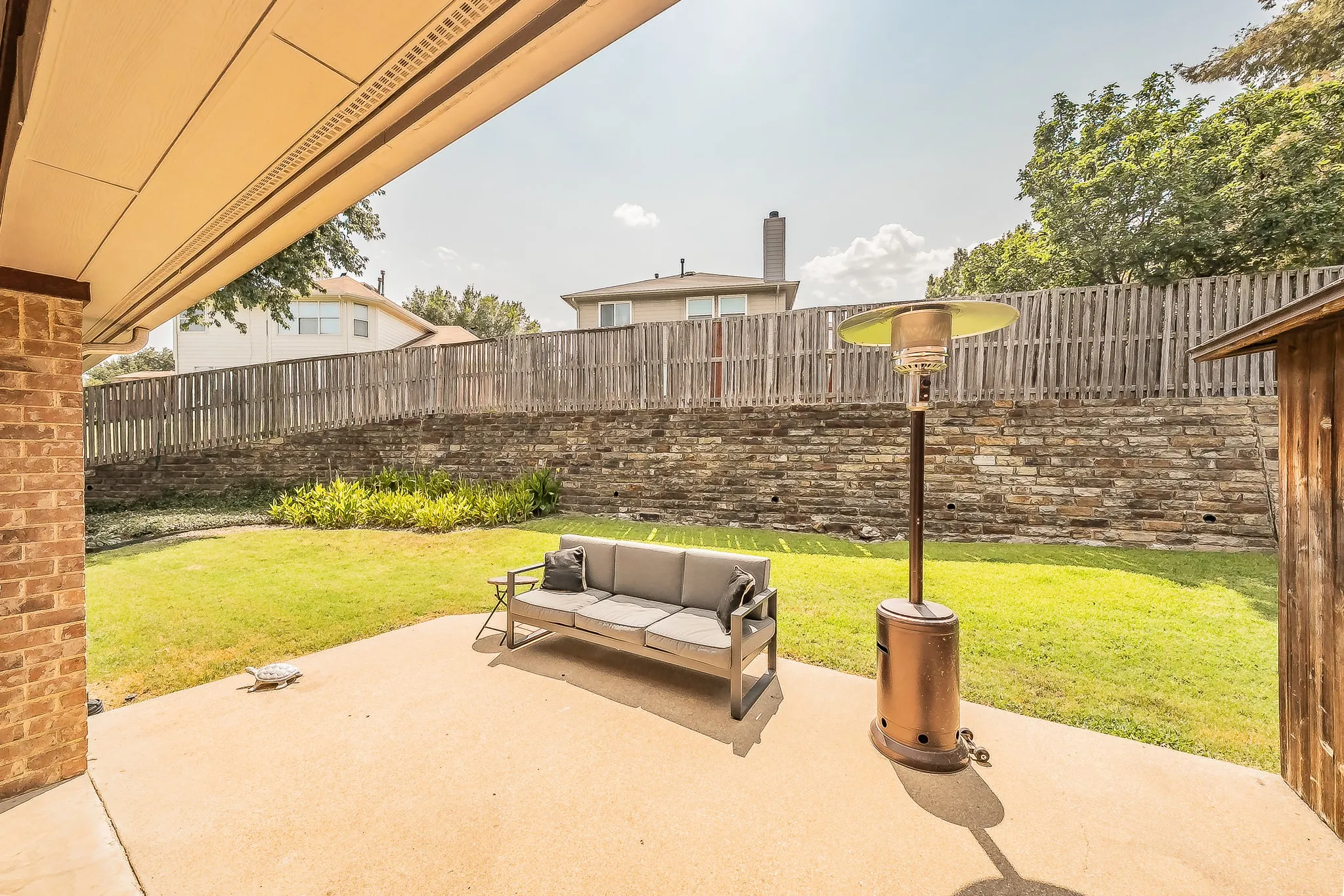 Covered patio with a concrete surface, brick exterior wall, and wood plank privacy fence