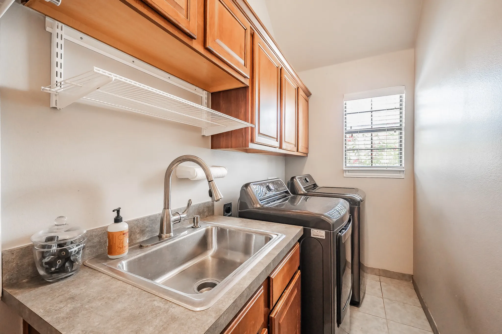 Laundry area featuring wood-finish cabinetry, a utility sink with a gooseneck faucet, a countertop, and tiled flooring