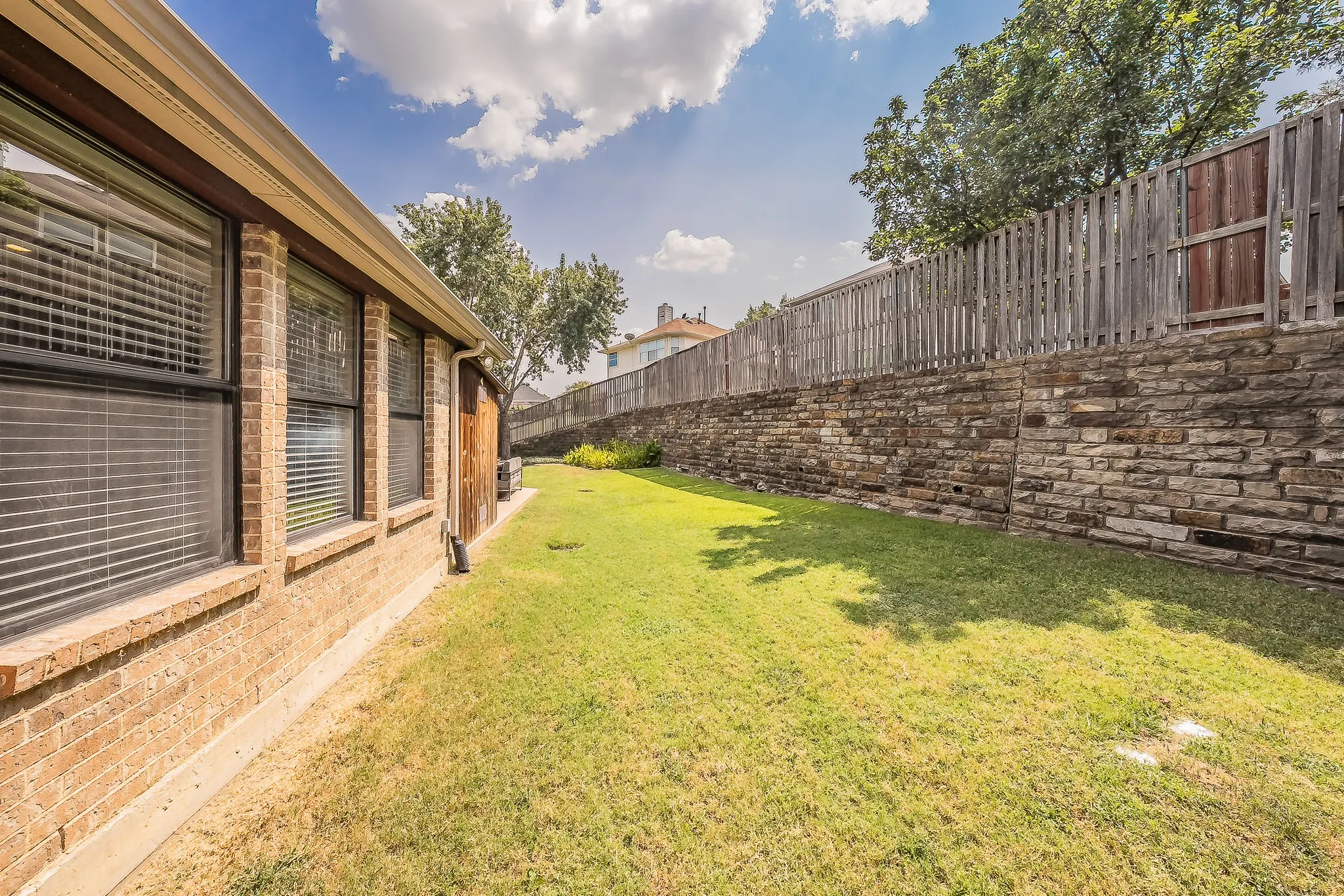 Expansive grassy area with a stone retaining wall, wood privacy fencing, and brick exterior