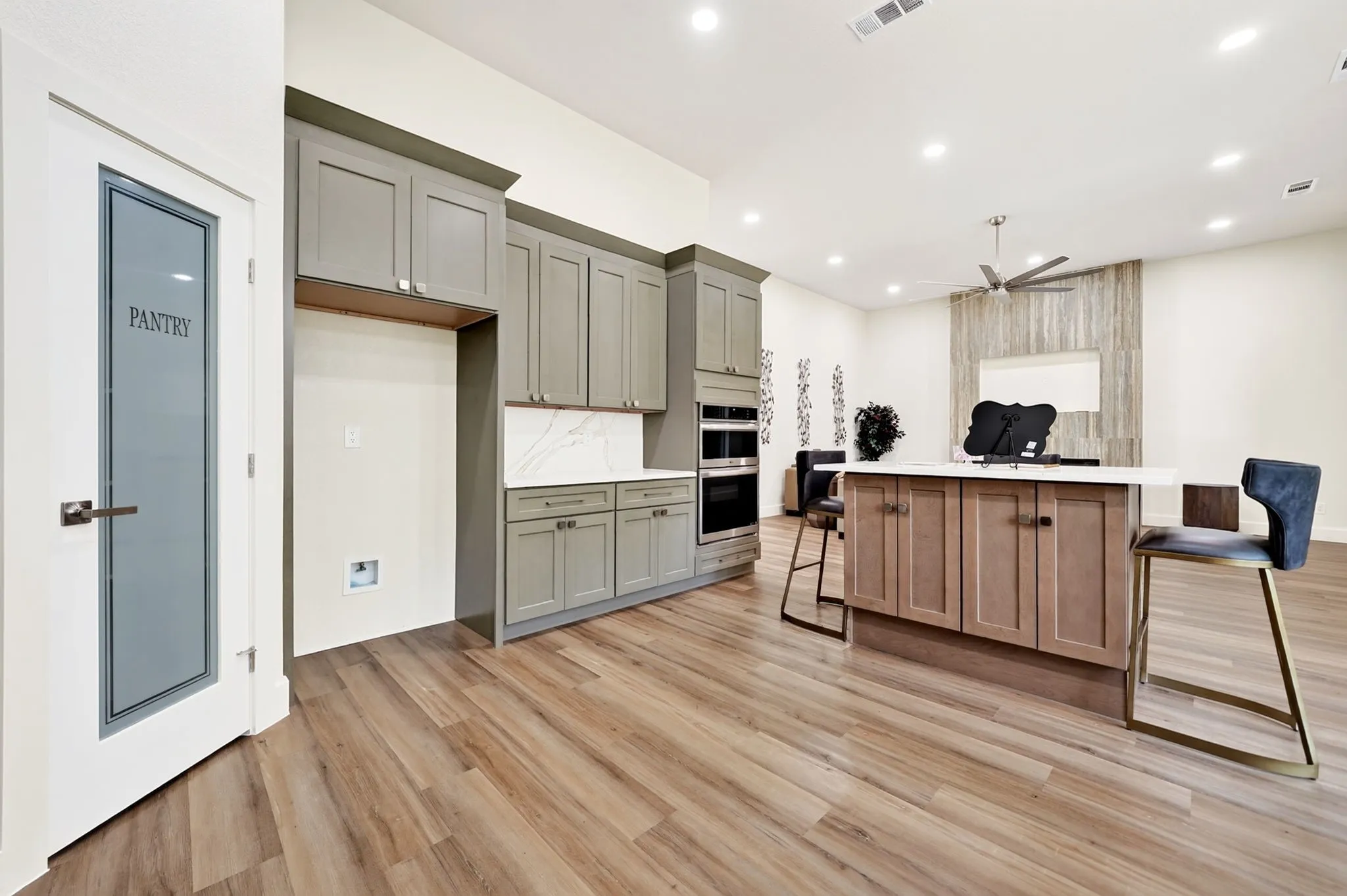 Wood-finish flooring throughout, pantry with frosted glass door, built-in stainless steel appliances, kitchen island with seating, and recessed lighting