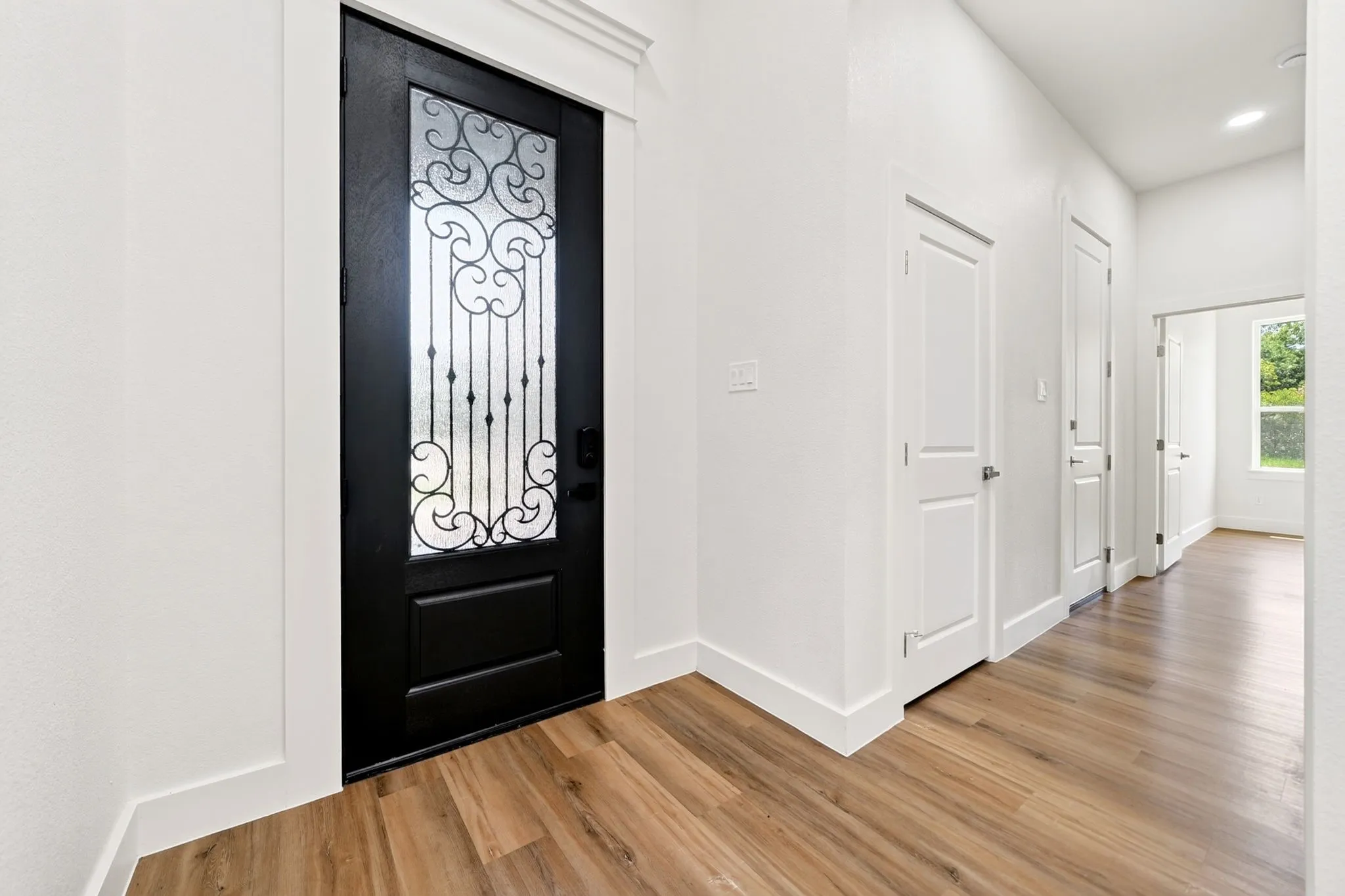 Decorative glass entry door with iron scrollwork, wood-finish flooring, and white interior walls