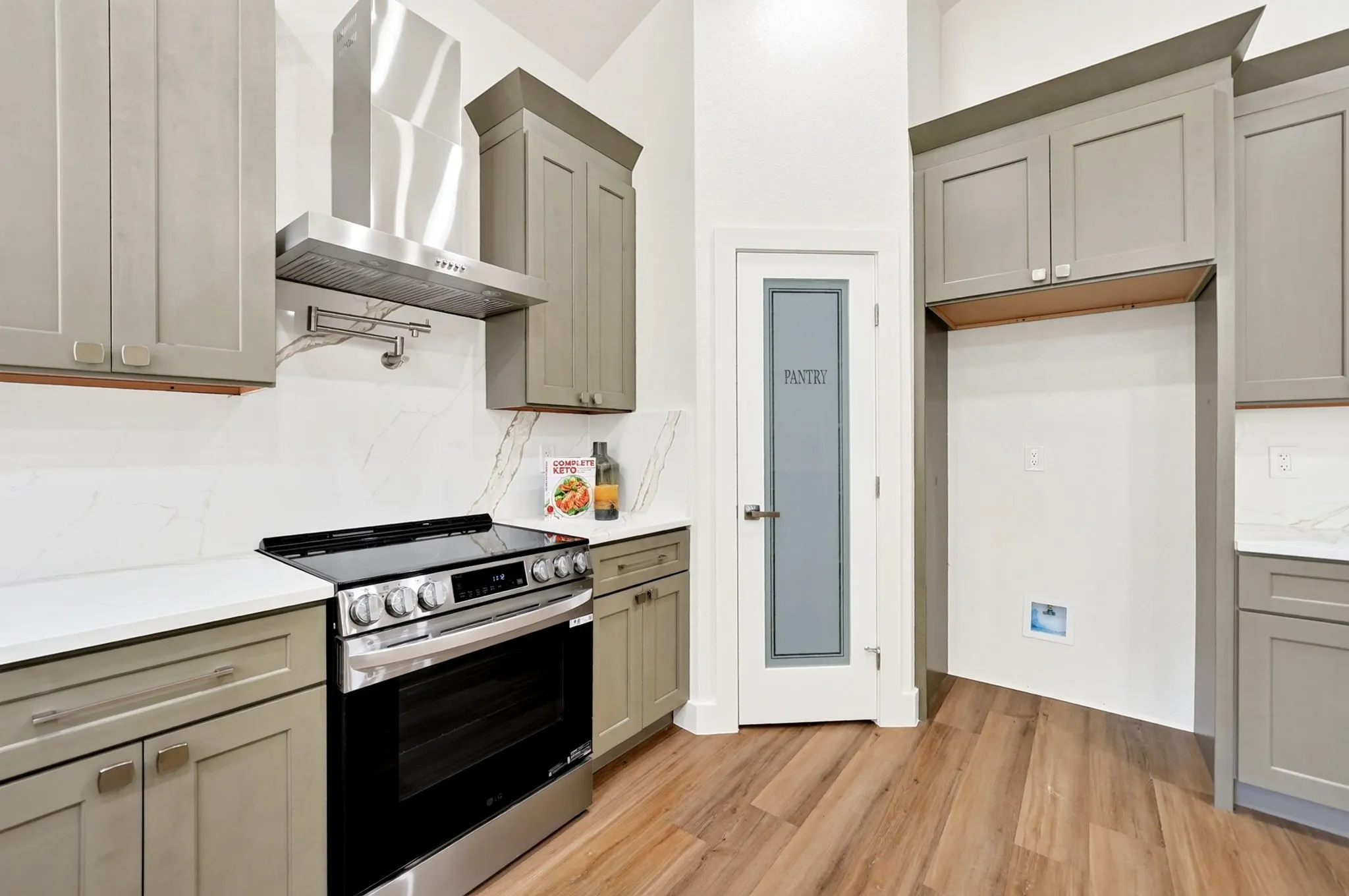 Modern kitchen featuring stainless steel appliances, a range hood, light-toned cabinetry, white countertops, and wood-finish flooring
