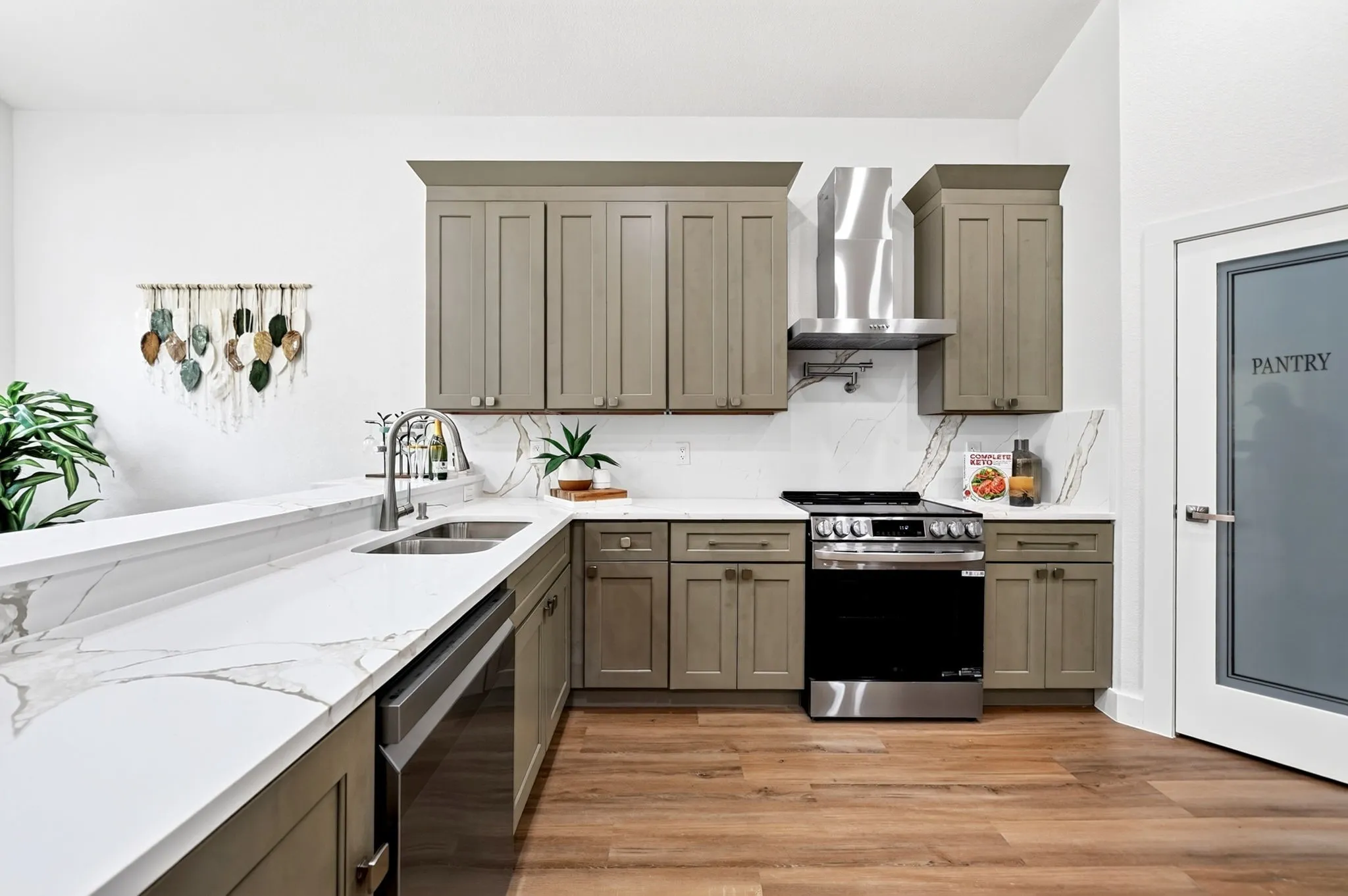 Kitchen featuring wood-finish flooring, white counters with veining, gray cabinetry, stainless steel appliances, and a pantry door with frosted glass