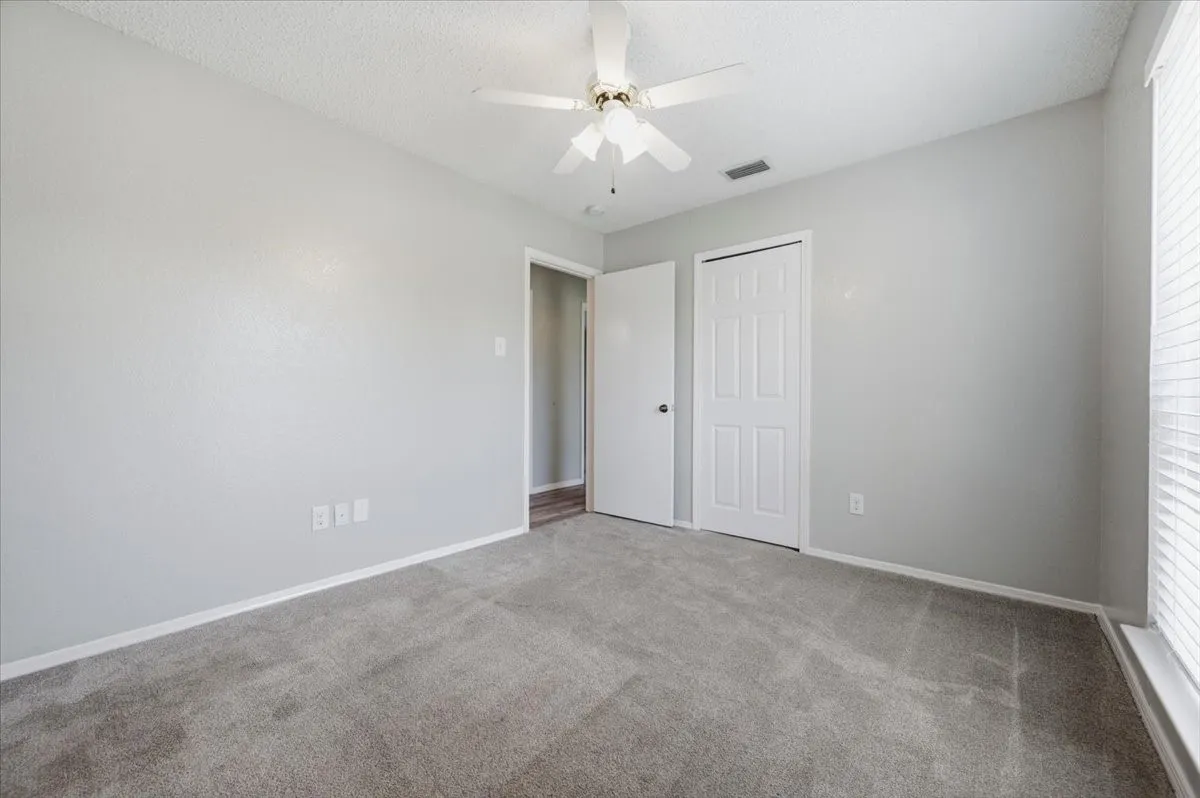 Secondary bedroom features a ceiling fan with light fixture and a reach-in closet. A doorway opens to the hallway beyond. Carpet flooring extends throughout.