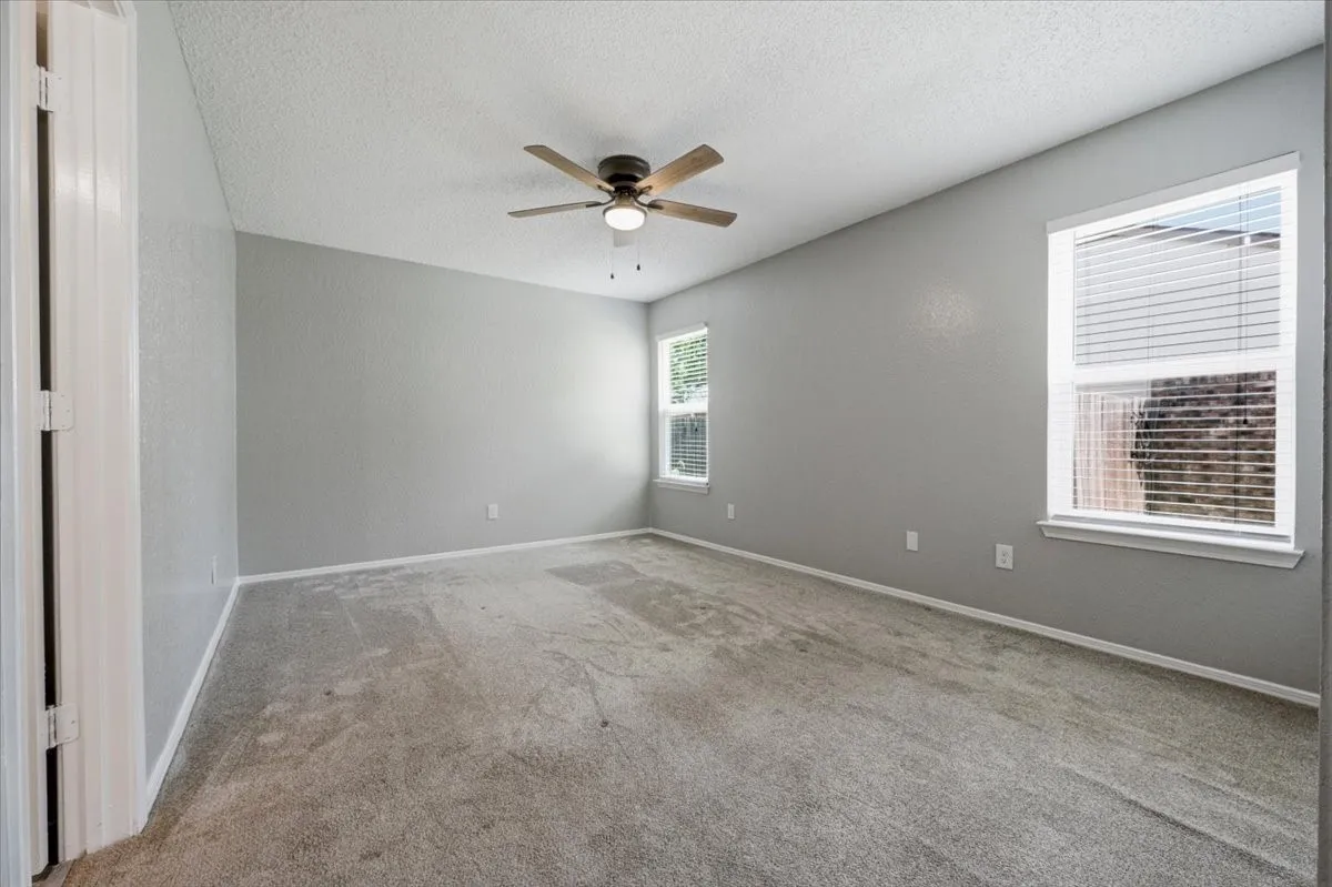 Primary bedroom features a ceiling fan with light fixture and two windows bringing in natural light. A closet is visible near the entry. Carpet flooring extends throughout.