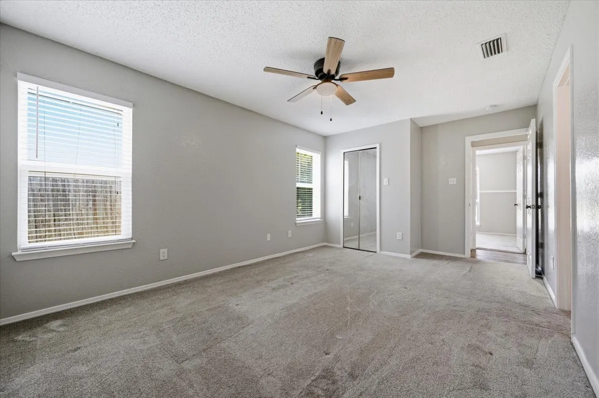 Primary bedroom features a ceiling fan with light fixture, two windows, and a mirrored sliding closet door. The layout connects to the adjoining ensuite bath. Carpet flooring extends throughout.