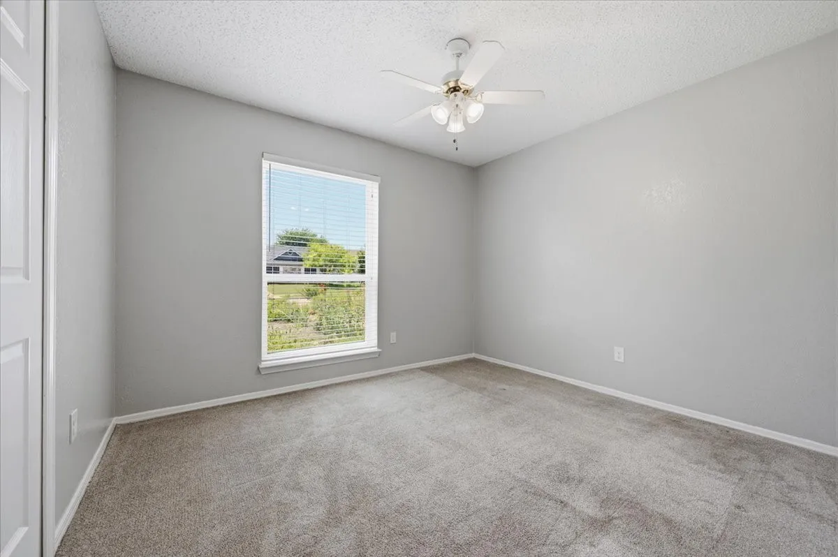 Secondary bedroom features a ceiling fan with light fixture and a single window overlooking the front yard. Carpet flooring extends throughout.
