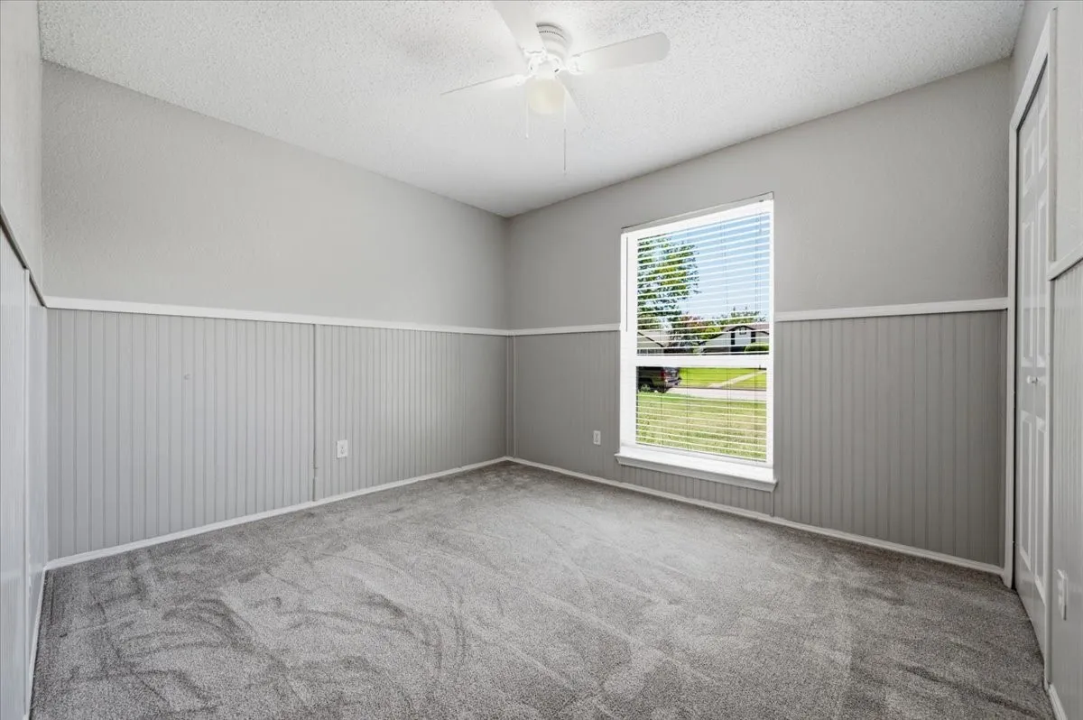 Secondary bedroom features a ceiling fan with light fixture, painted wainscoting along the lower walls, and a window overlooking the front yard. A closet is positioned near the entry. Carpet flooring extends throughout.
