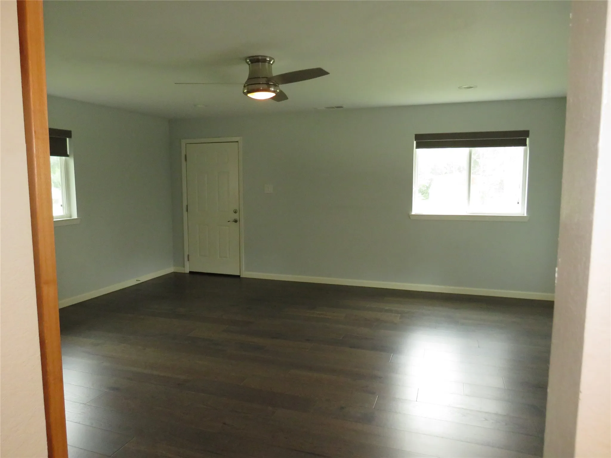 Wood-finish flooring, light grey walls, and a ceiling fan with integrated lighting