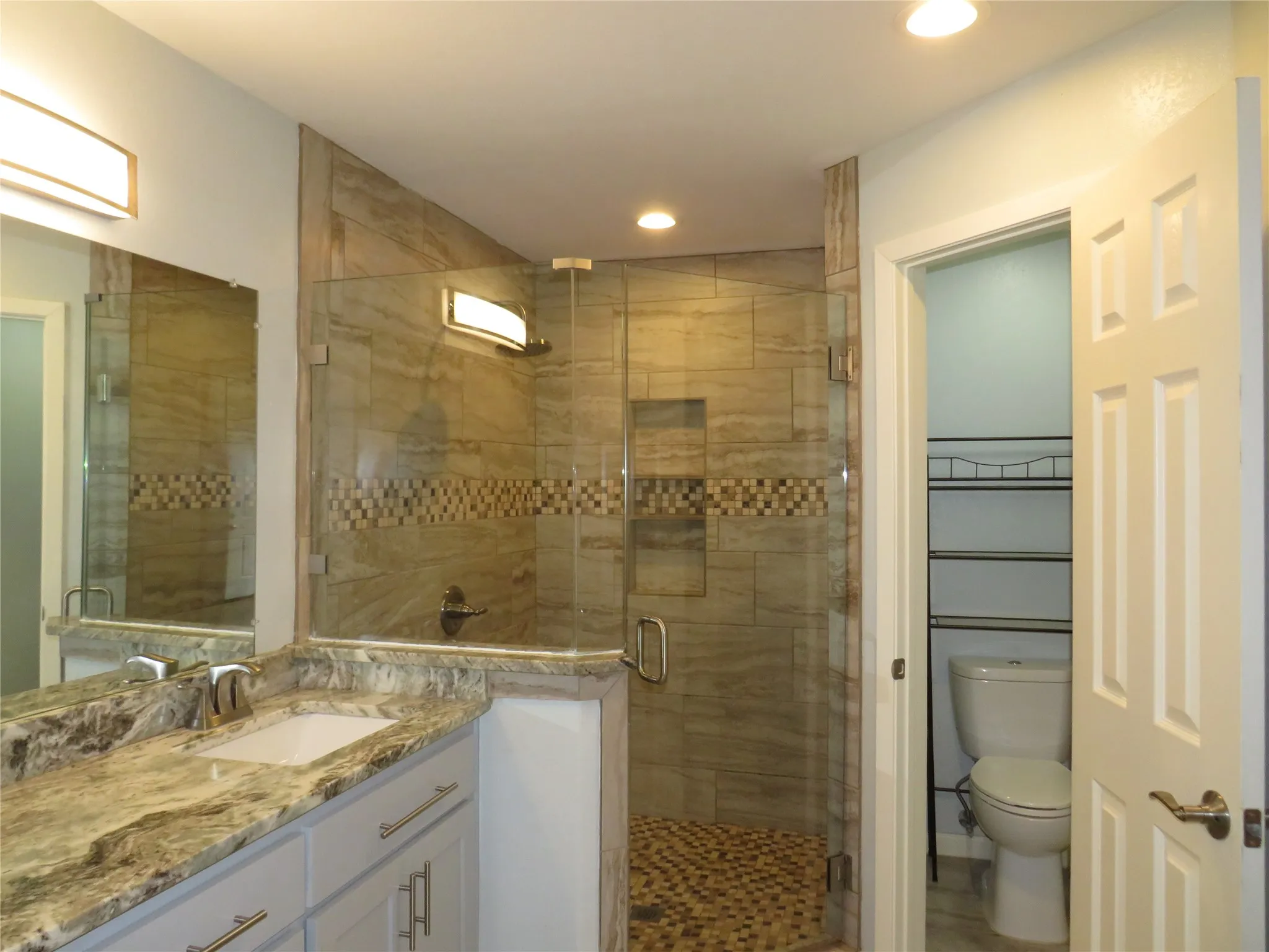 Glass-enclosed shower with tiled walls and pebble-finish flooring