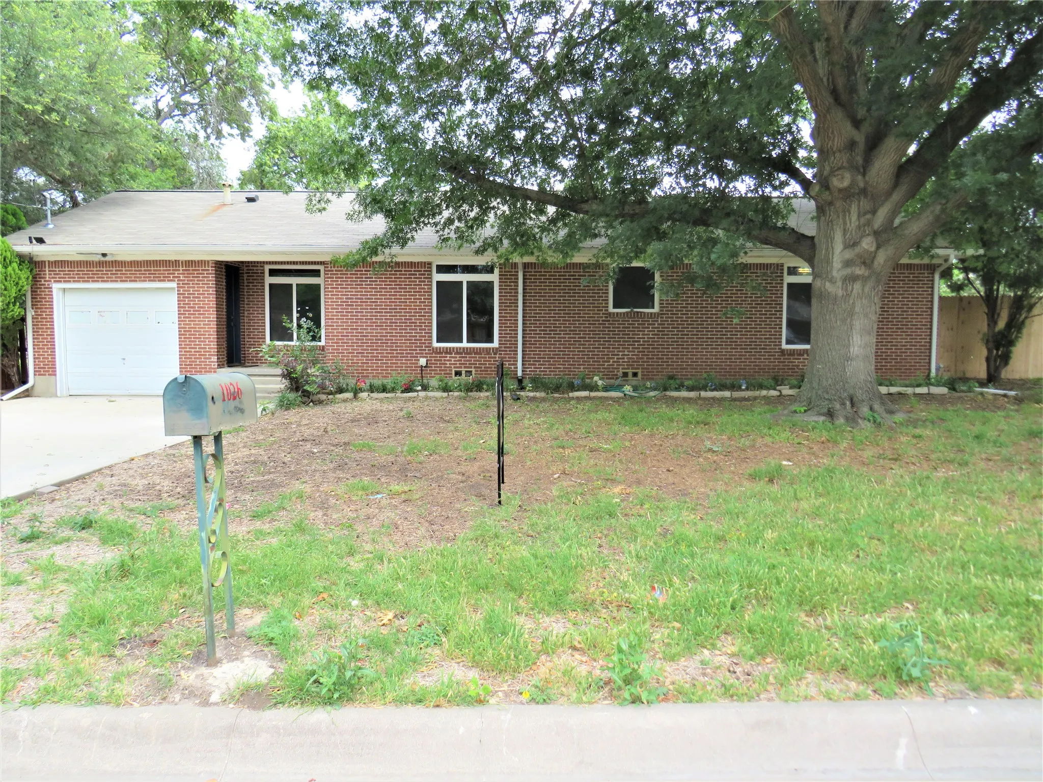 Brick exterior with white-framed windows, an attached garage, a mature front tree, and a concrete driveway