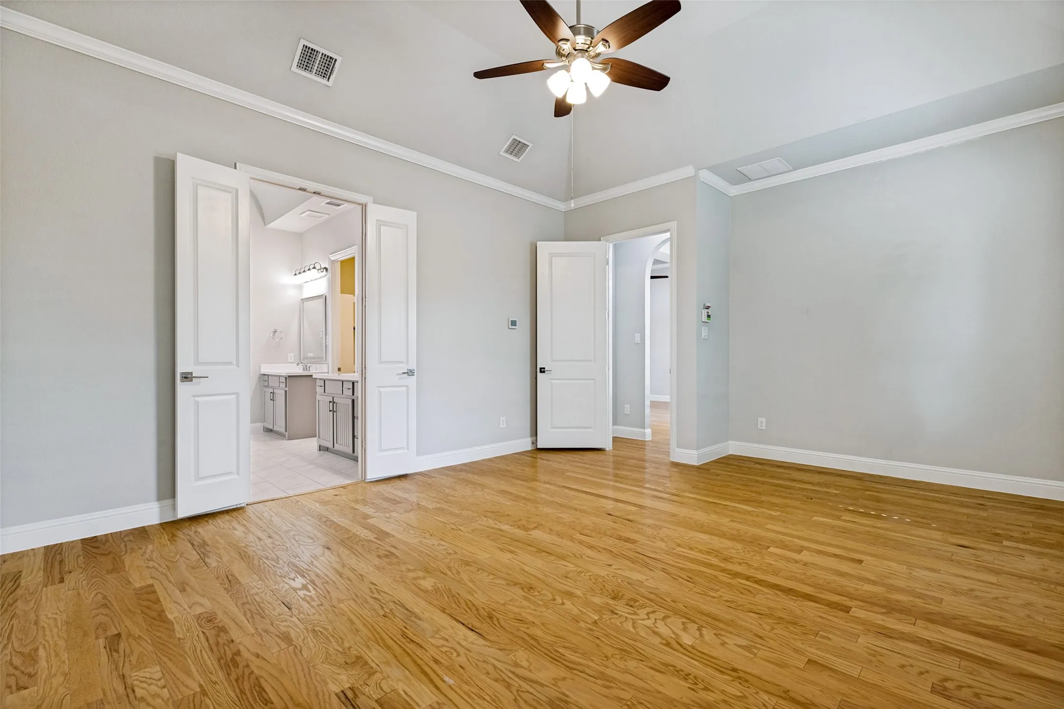 Vaulted ceiling with a ceiling fan, wood-finish flooring, white double doors, crown molding, and light gray wall paint